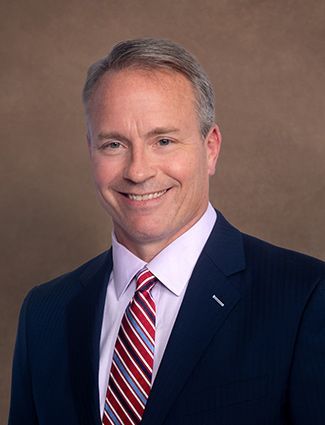 A smiling doctor in a lab coat with a stethoscope around his neck.