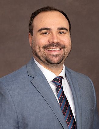 A smiling doctor in a lab coat with a stethoscope around his neck.