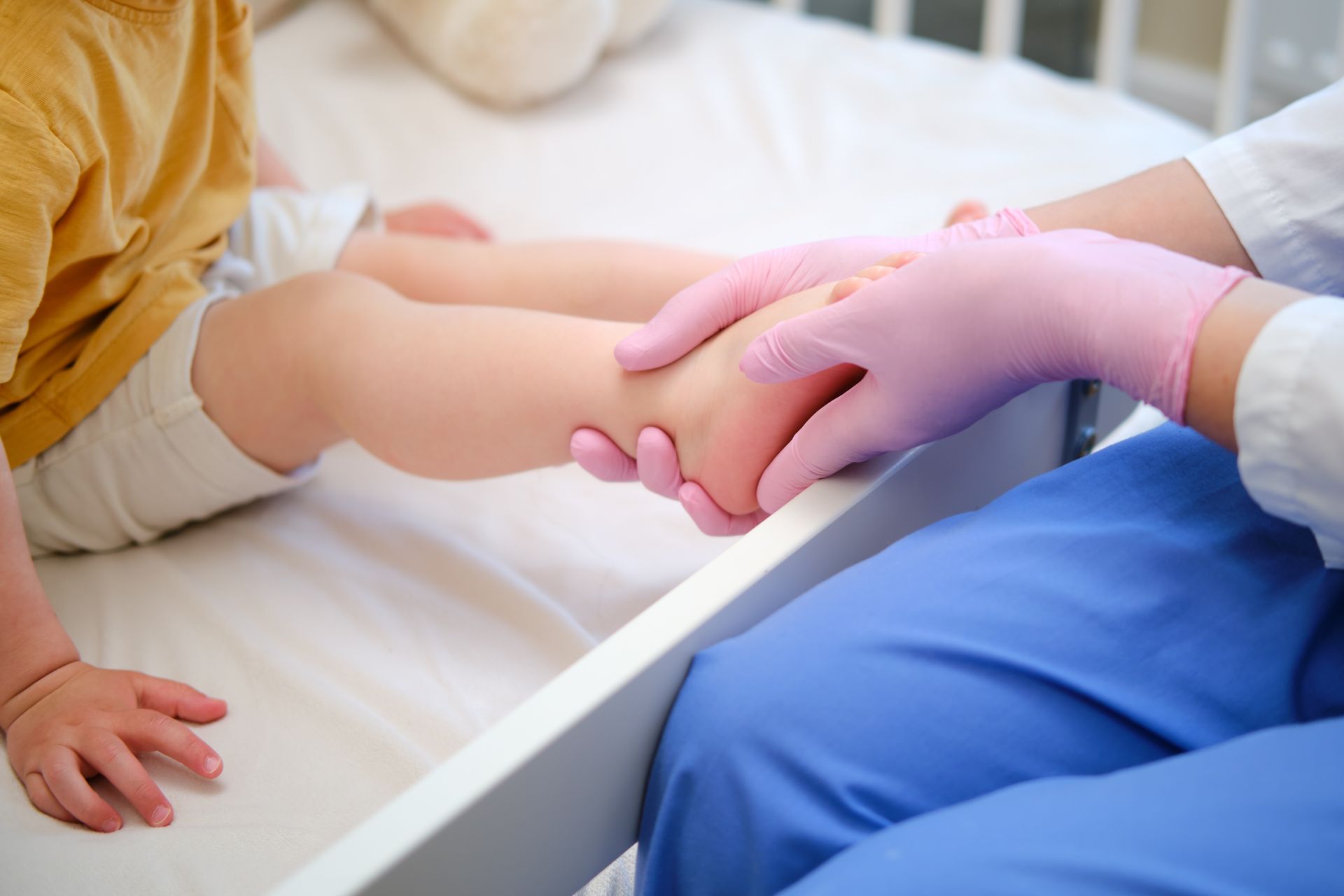 Child's leg being examined by a person wearing pink gloves, on a bed.