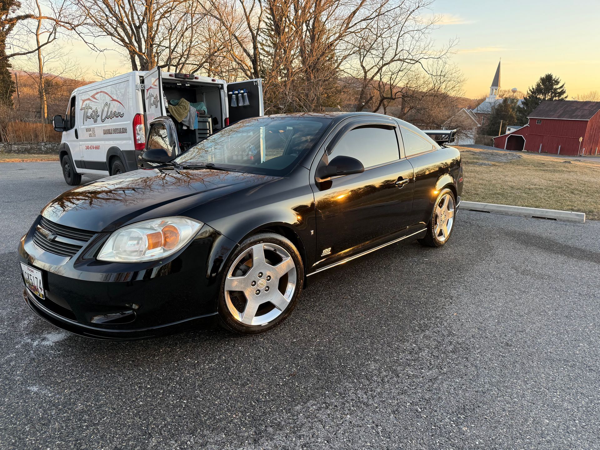 A black car is parked on the side of the road next to a white van.