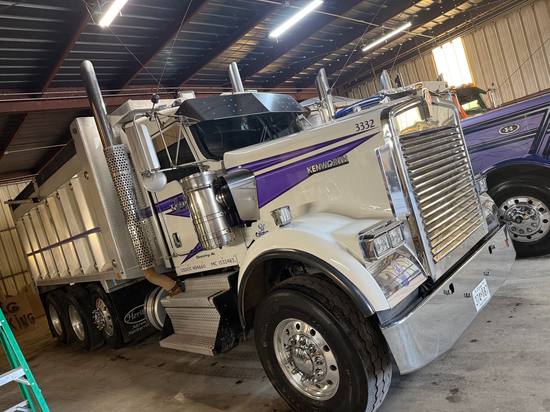 A white and purple dump truck is parked in a garage.