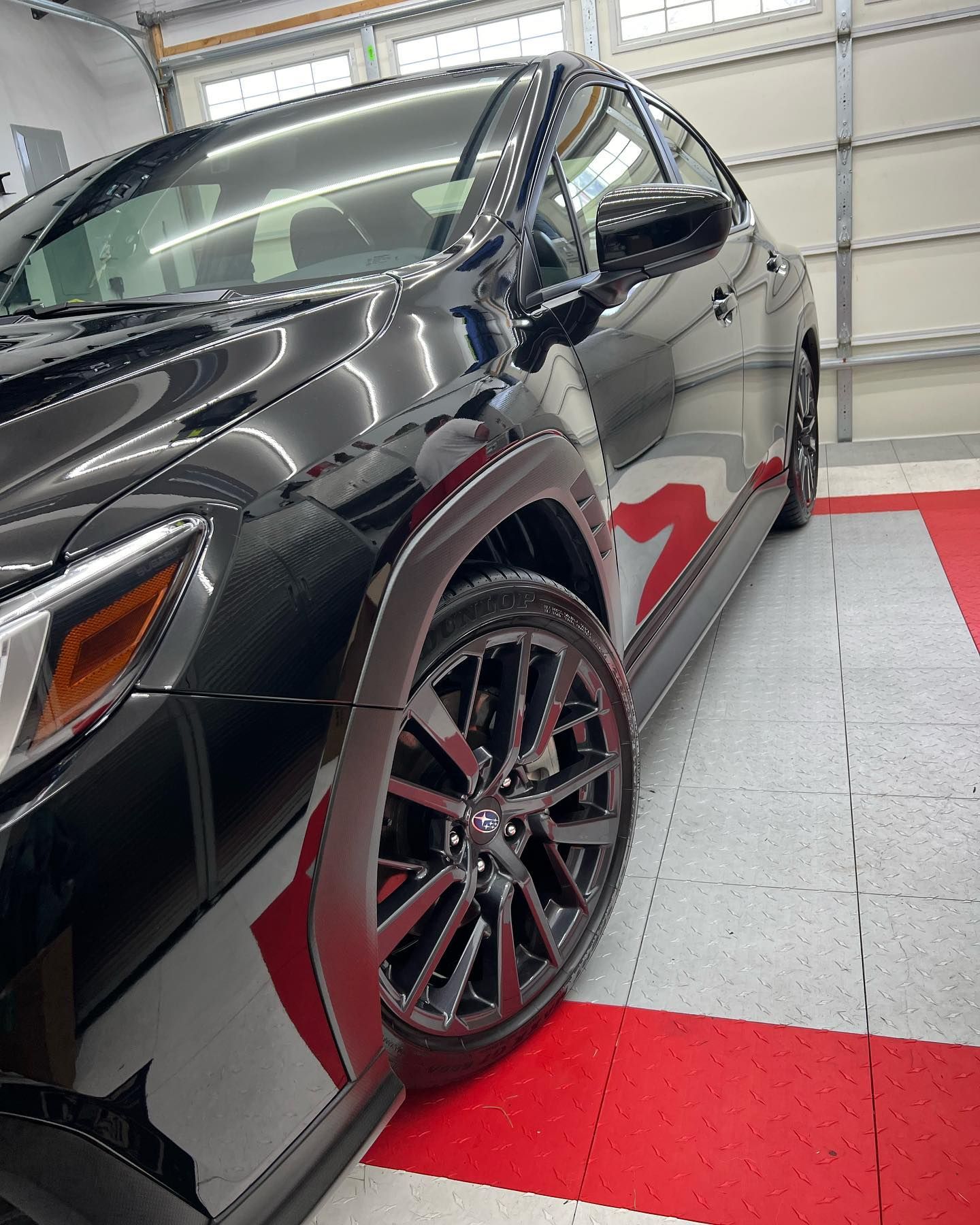 A black car is parked in a garage on a red and white tile floor.