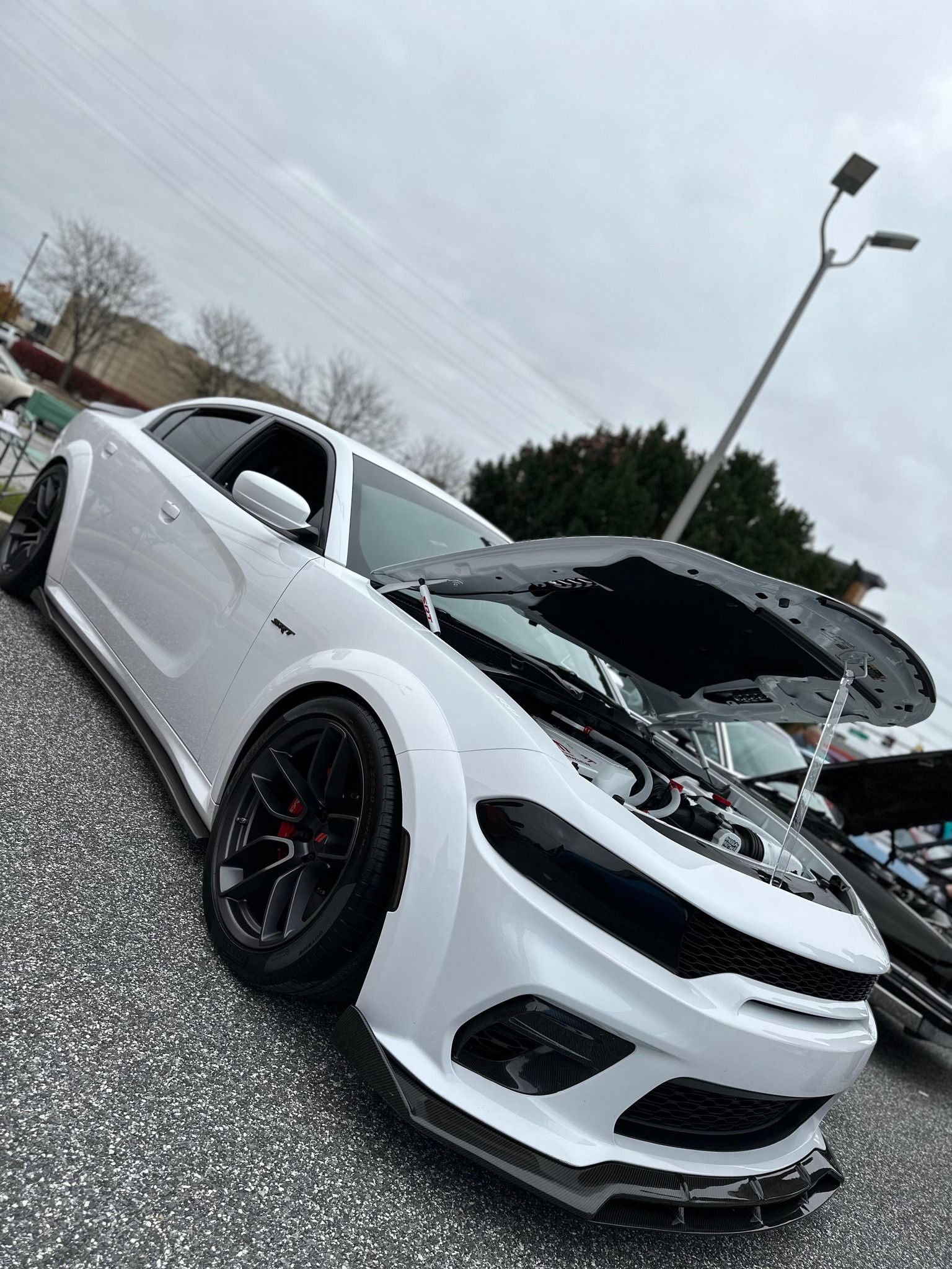 A white car with the hood up is parked in a parking lot.