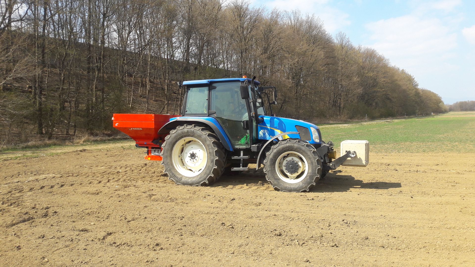 Ein blauer Traktor pflügt ein Feld mit Bäumen im Hintergrund.