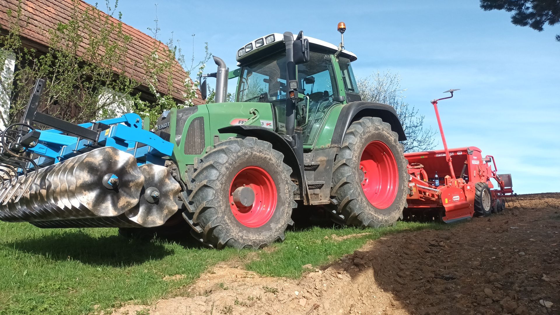 Ein grüner Traktor mit roten Rädern pflügt ein Feld.