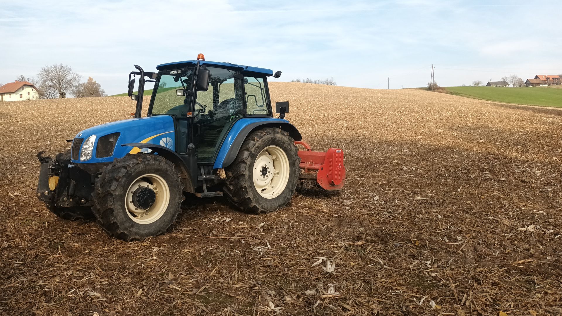 Ein blauer Traktor mit einem daran befestigten Pflug pflügt ein Feld.