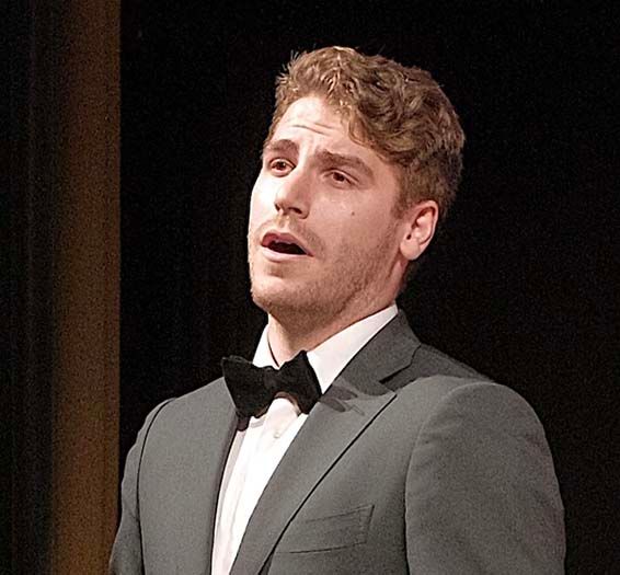 A man in a suit and bow tie is singing on a stage.