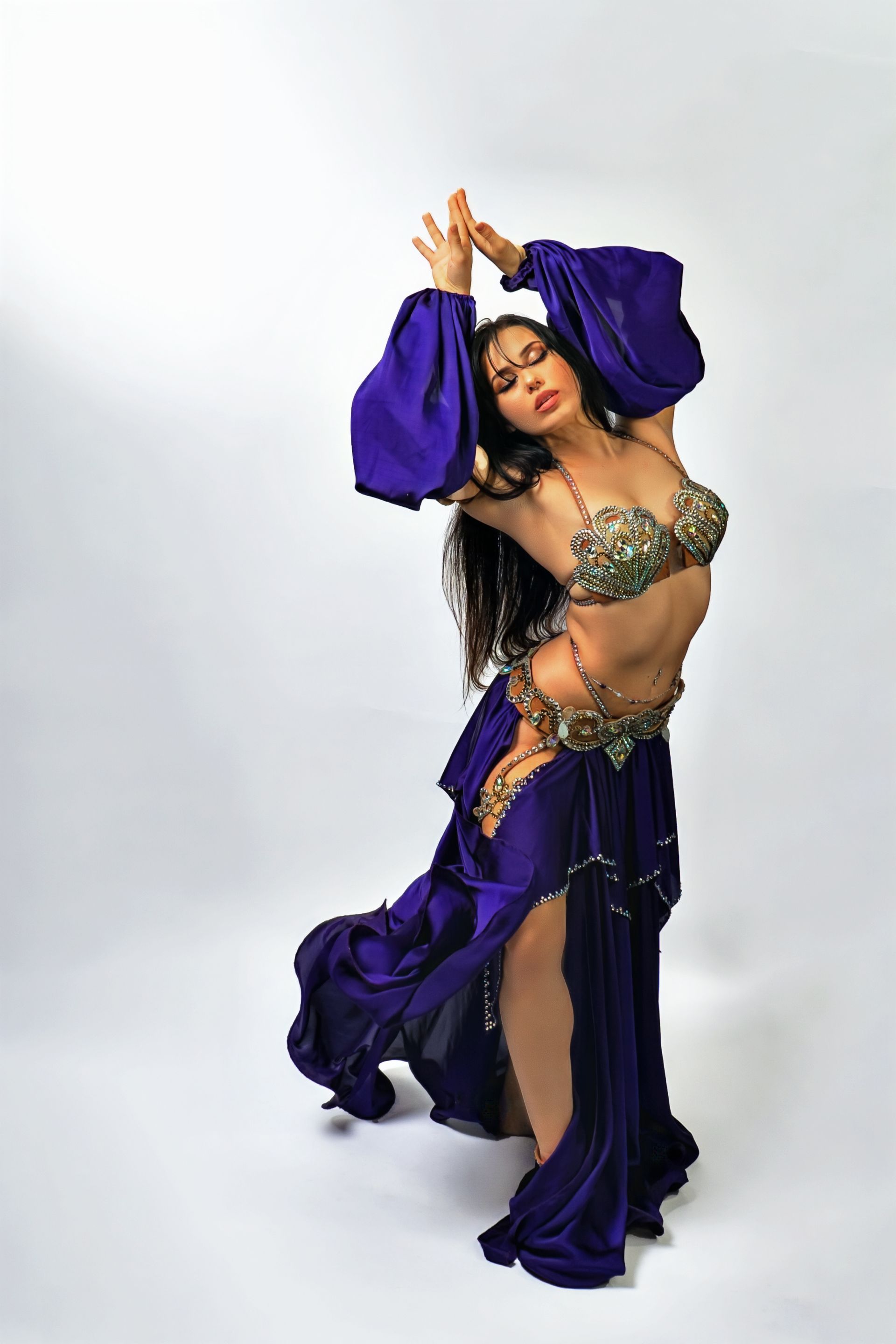 Belly dancer Azeeria Azizah in a purple dress is dancing on a white background.