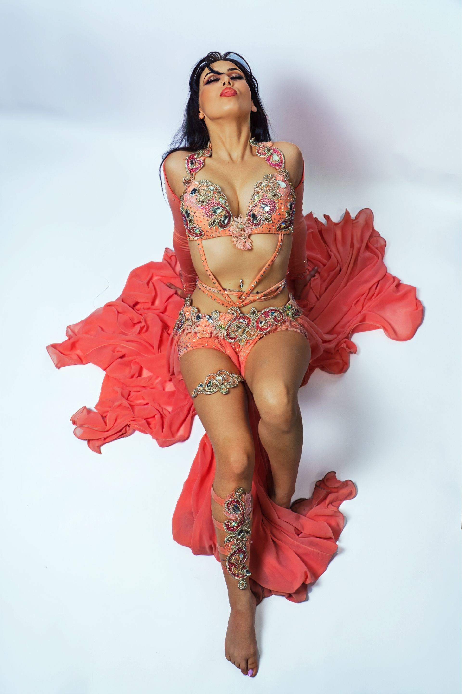Belly dancer Azeeria Azizah in a belly dancer costume is laying on the floor.