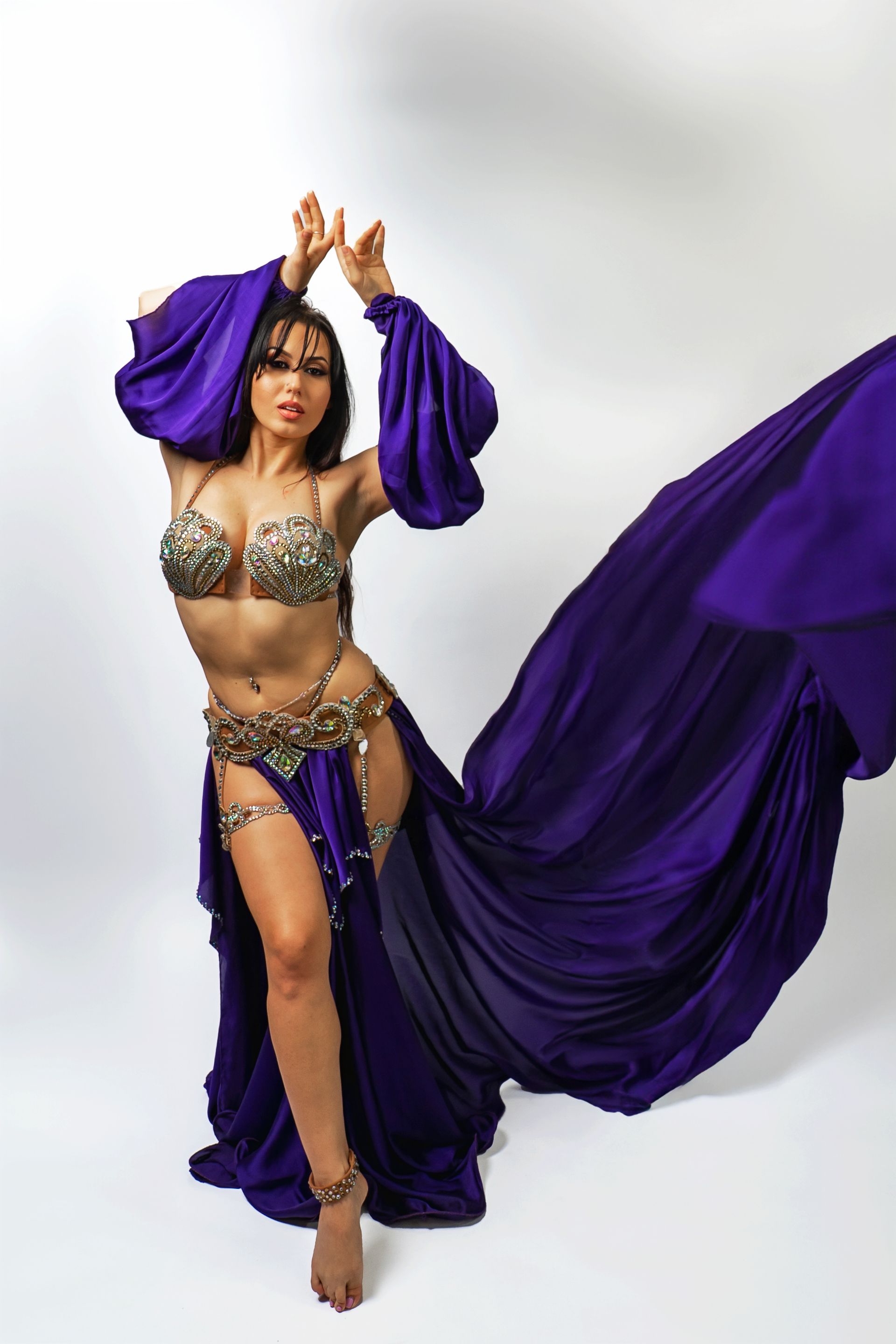Belly dancer Azeeria Azizah in a purple dress is dancing in front of a white background.