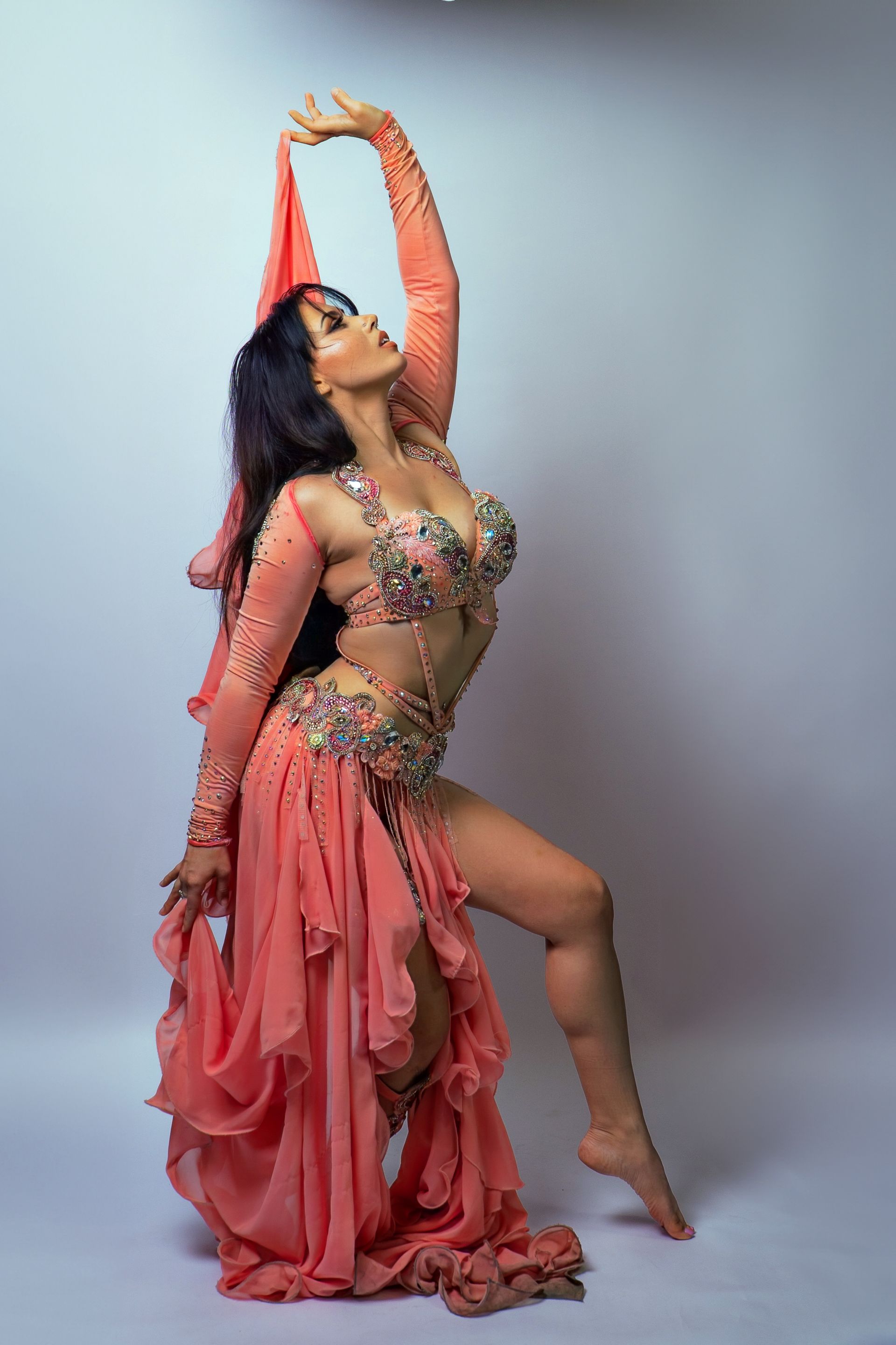 Belly dancer Azeeria Azizah in a pink dress is standing on one leg.