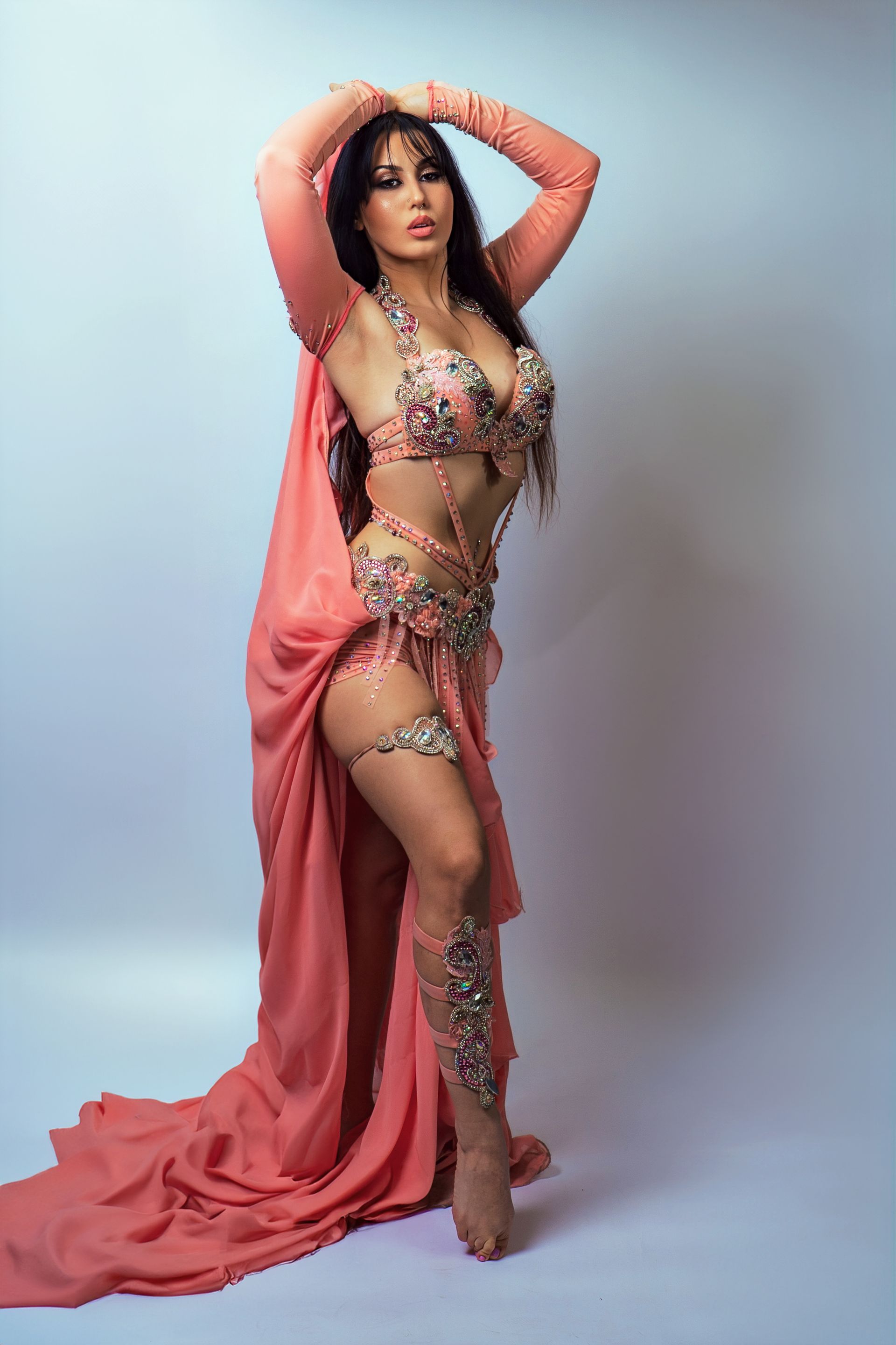 Belly dancer Azeeria Azizah in a pink belly dancer costume is standing in front of a white background.