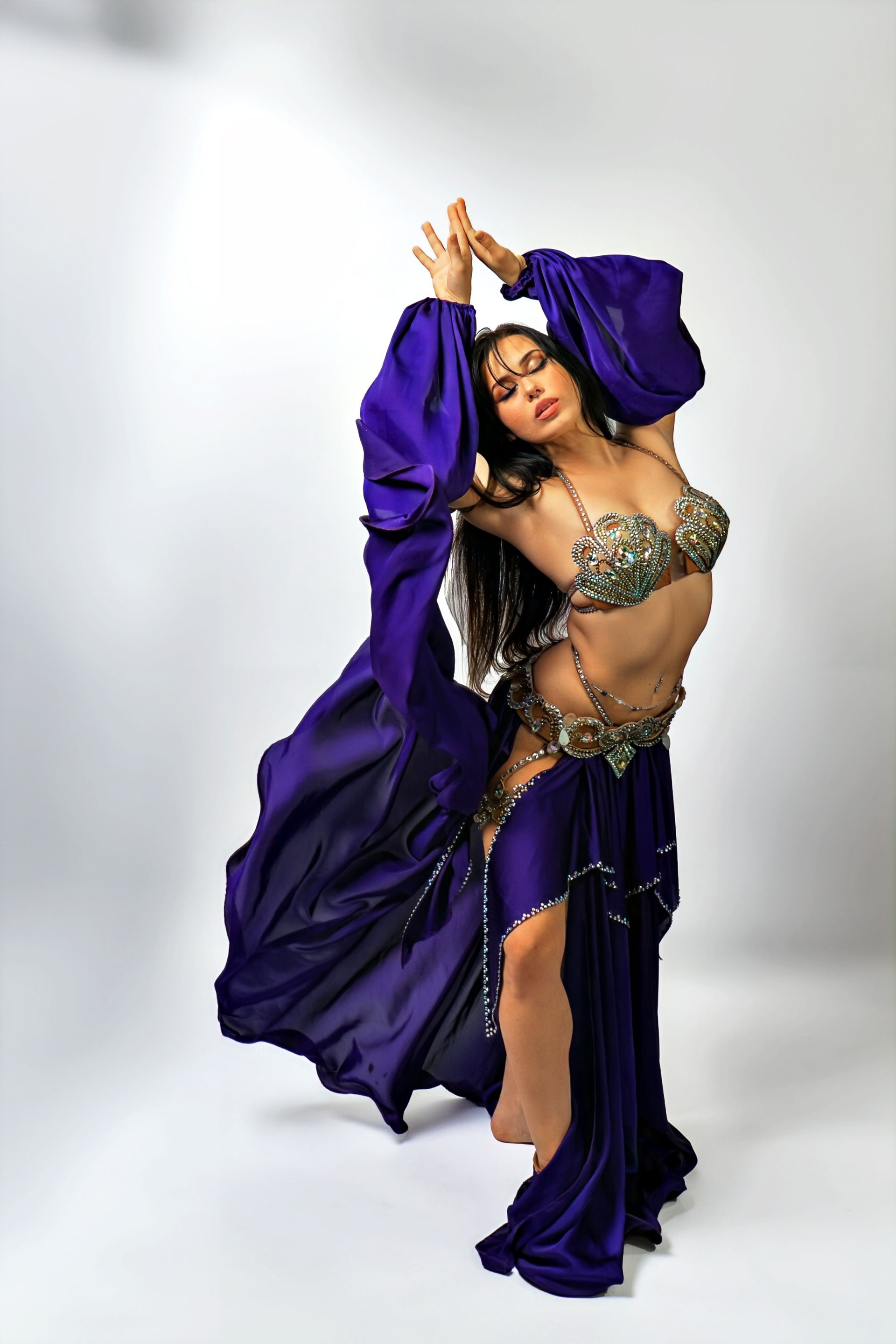 Belly dancer Azeeria Azizah in a purple dress is dancing on a white background.