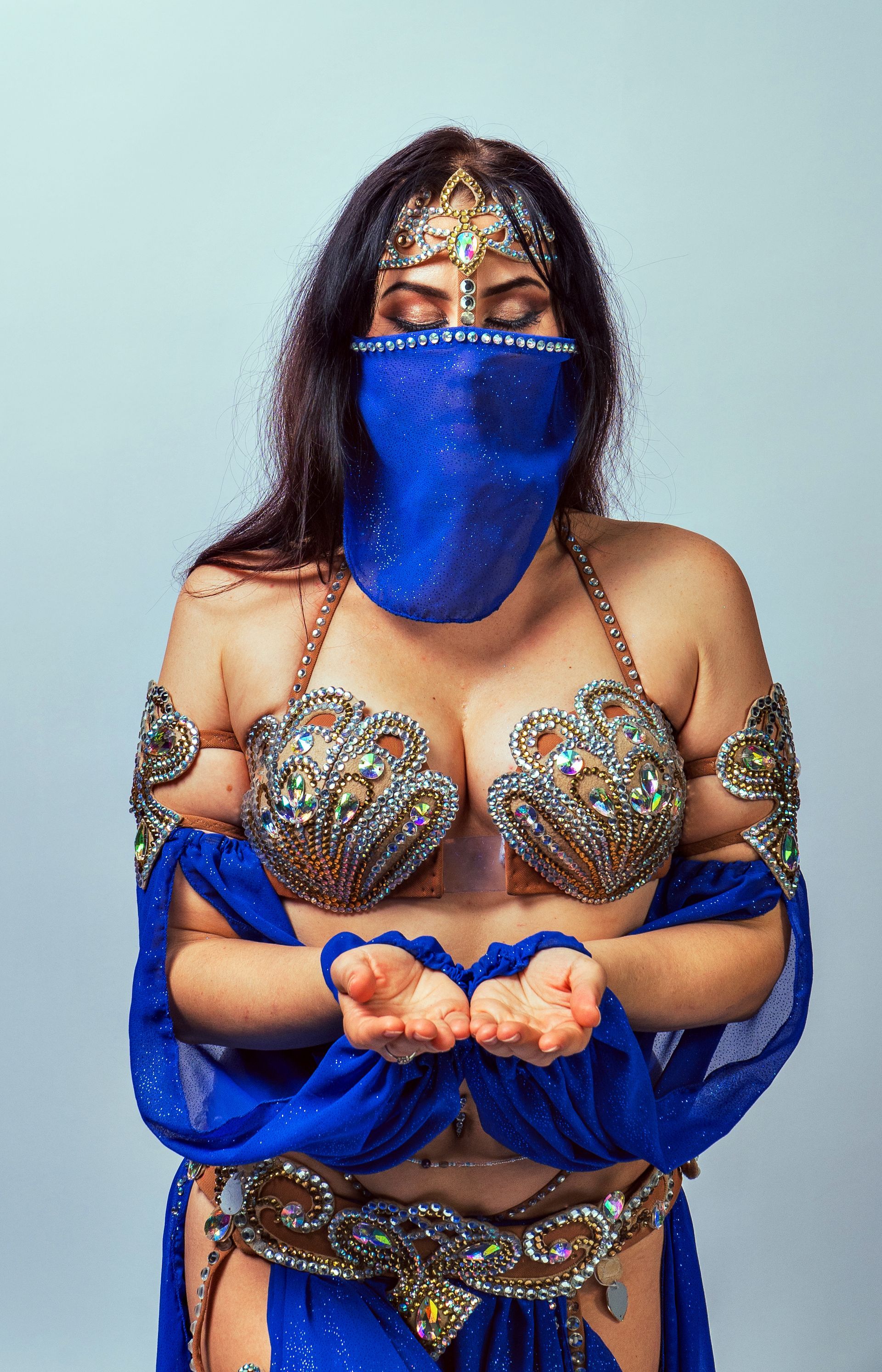Belly dancer Azeeria Azizah in a belly dancer costume is wearing a blue veil over her face.