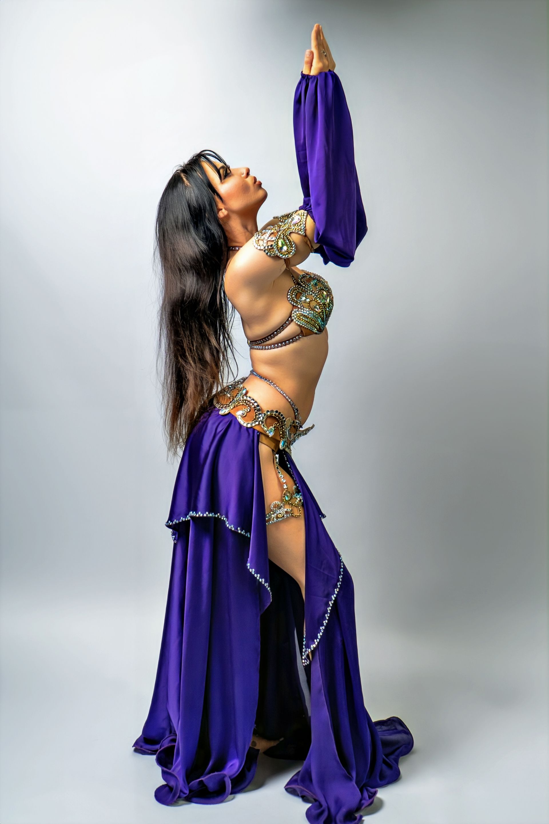 Belly dancer Azeeria Azizah in a purple dress is standing in a pose.