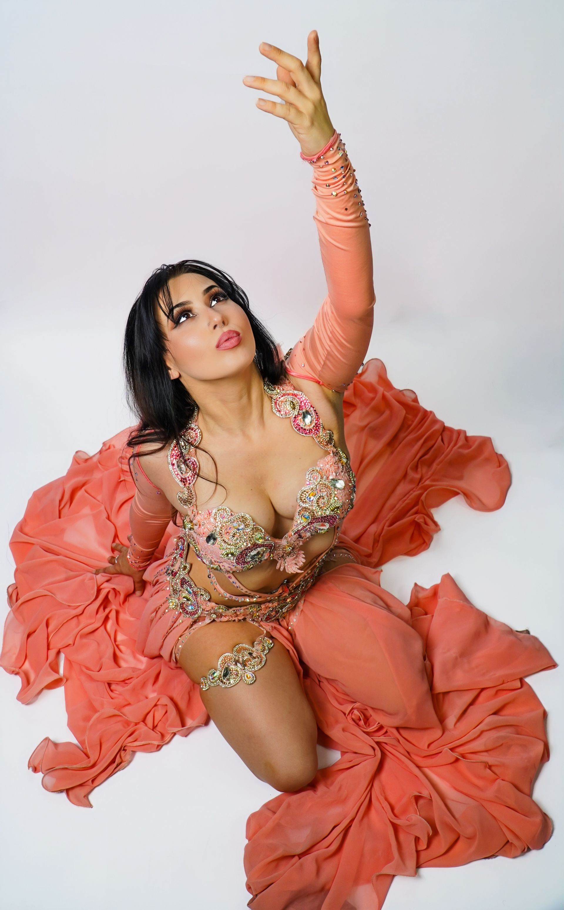 Belly dancer Azeeria Azizah in a belly dancer costume is kneeling on the floor.