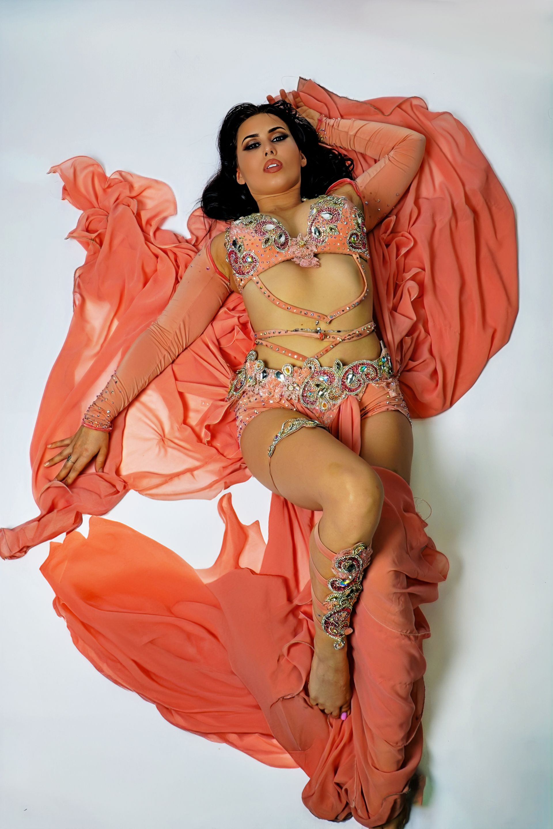 Belly dancer Azeeria Azizah in a belly dancer costume is laying on the floor.