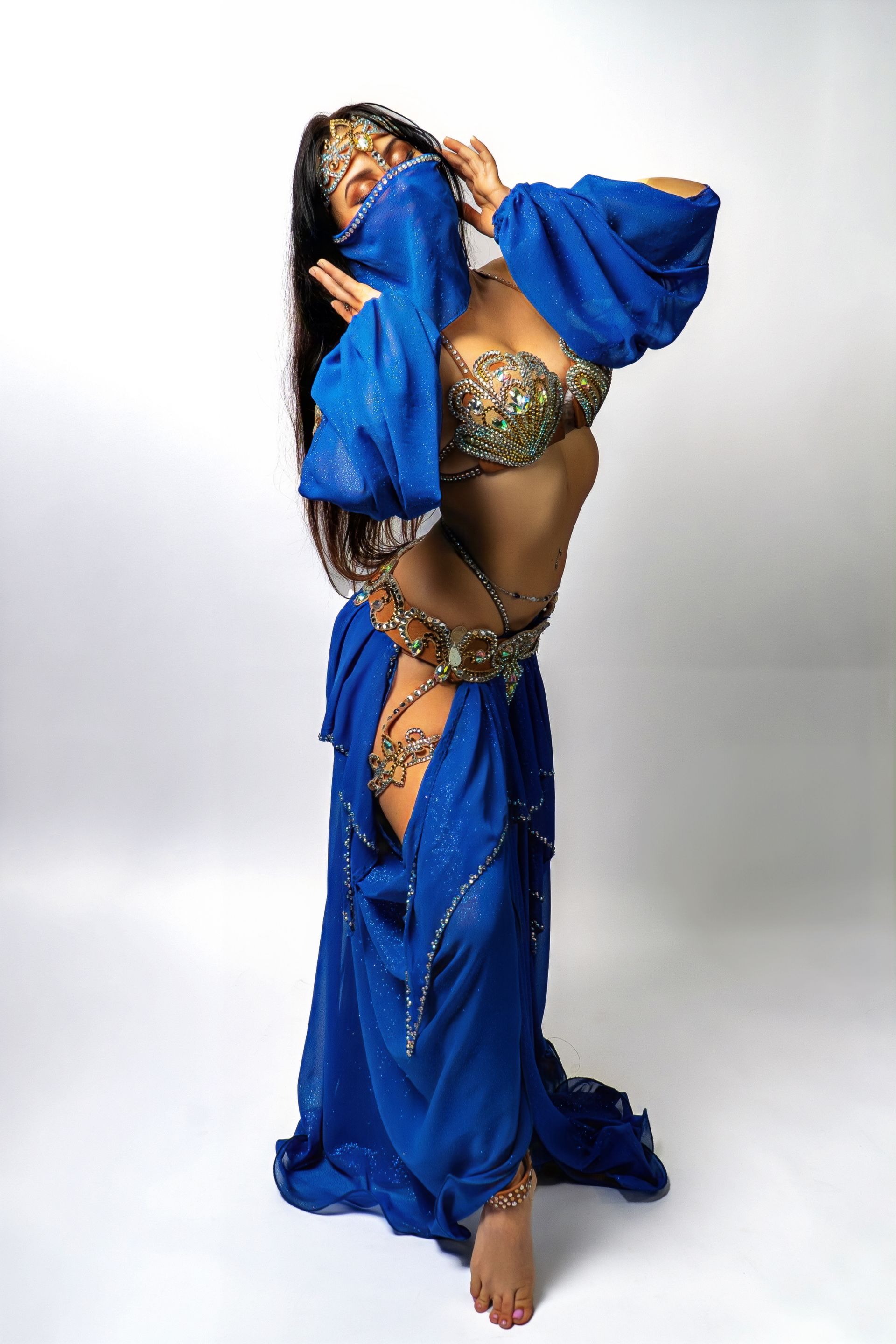 Belly dancer Azeeria Azizah in a blue dress is standing on a white background.