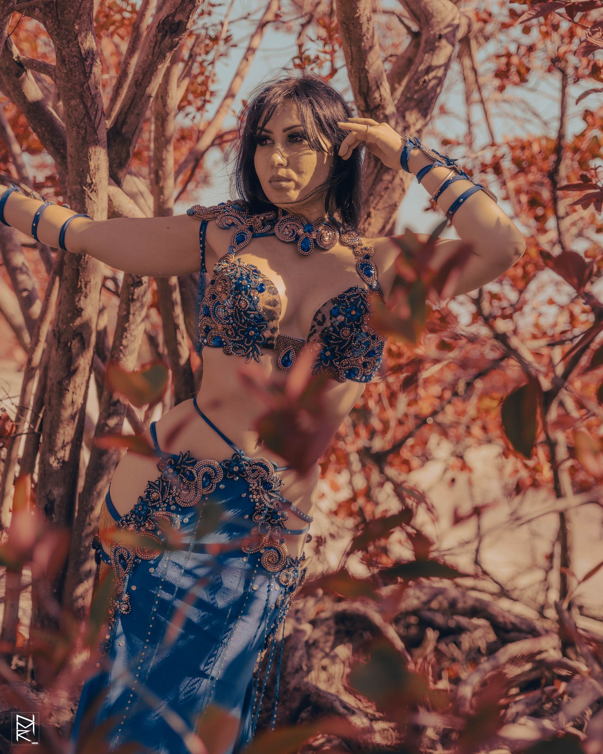 Belly dancer Azeeria Azizah in a belly dancer costume is standing in the woods.