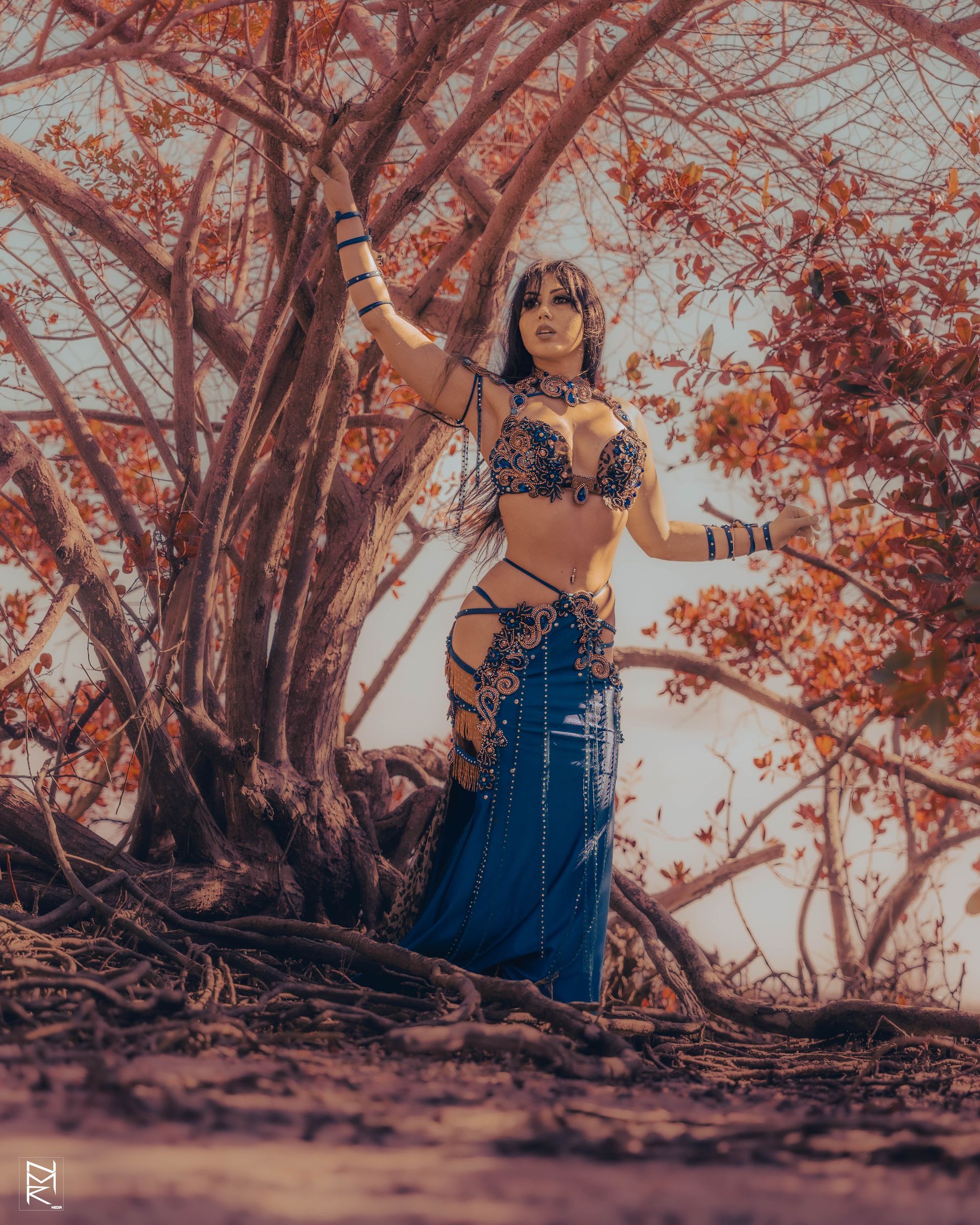 Azeeria Azizah in a blue belly dancer costume standing next to a tree.