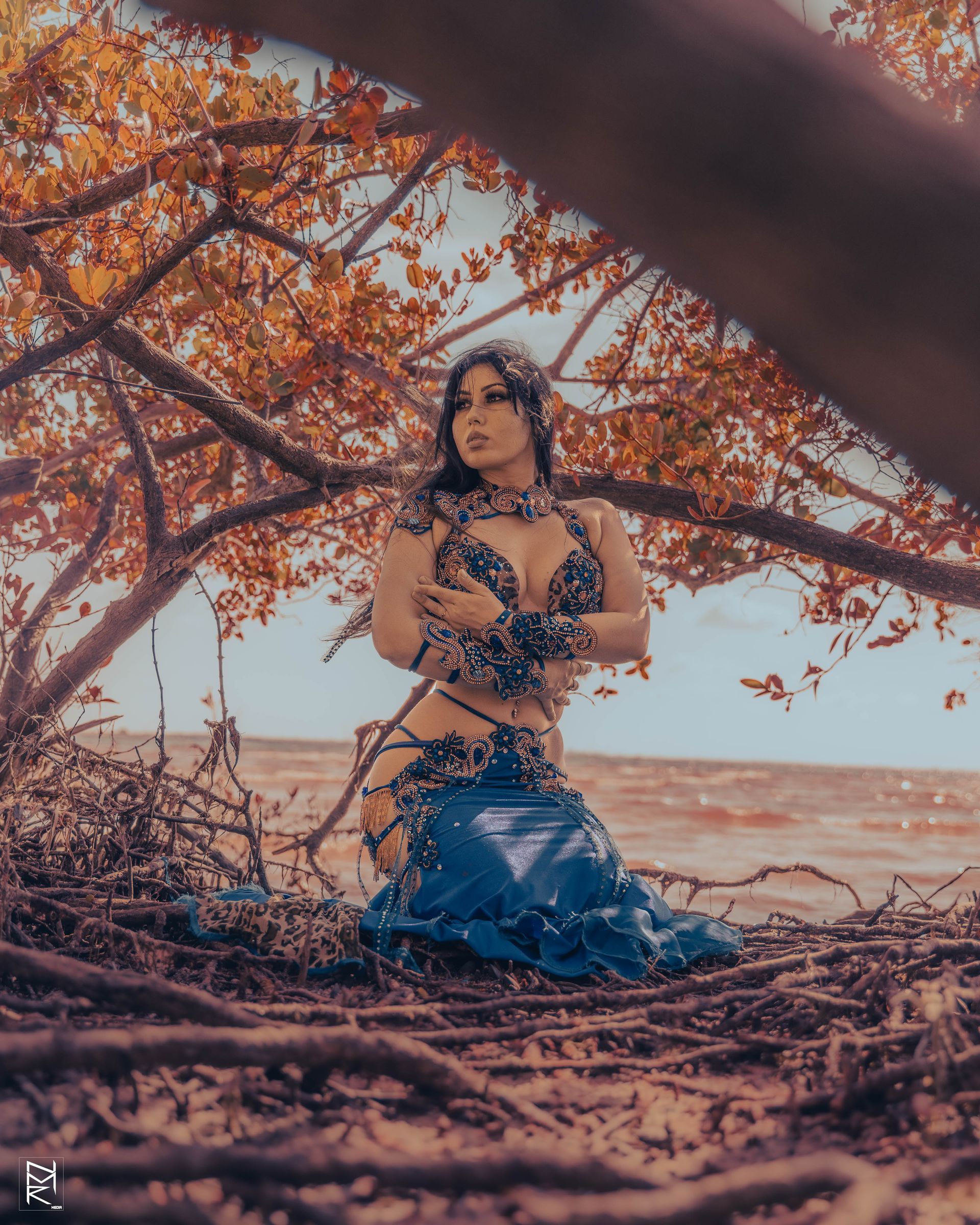 Azeeria Azizah in a blue dress kneeling under a tree.