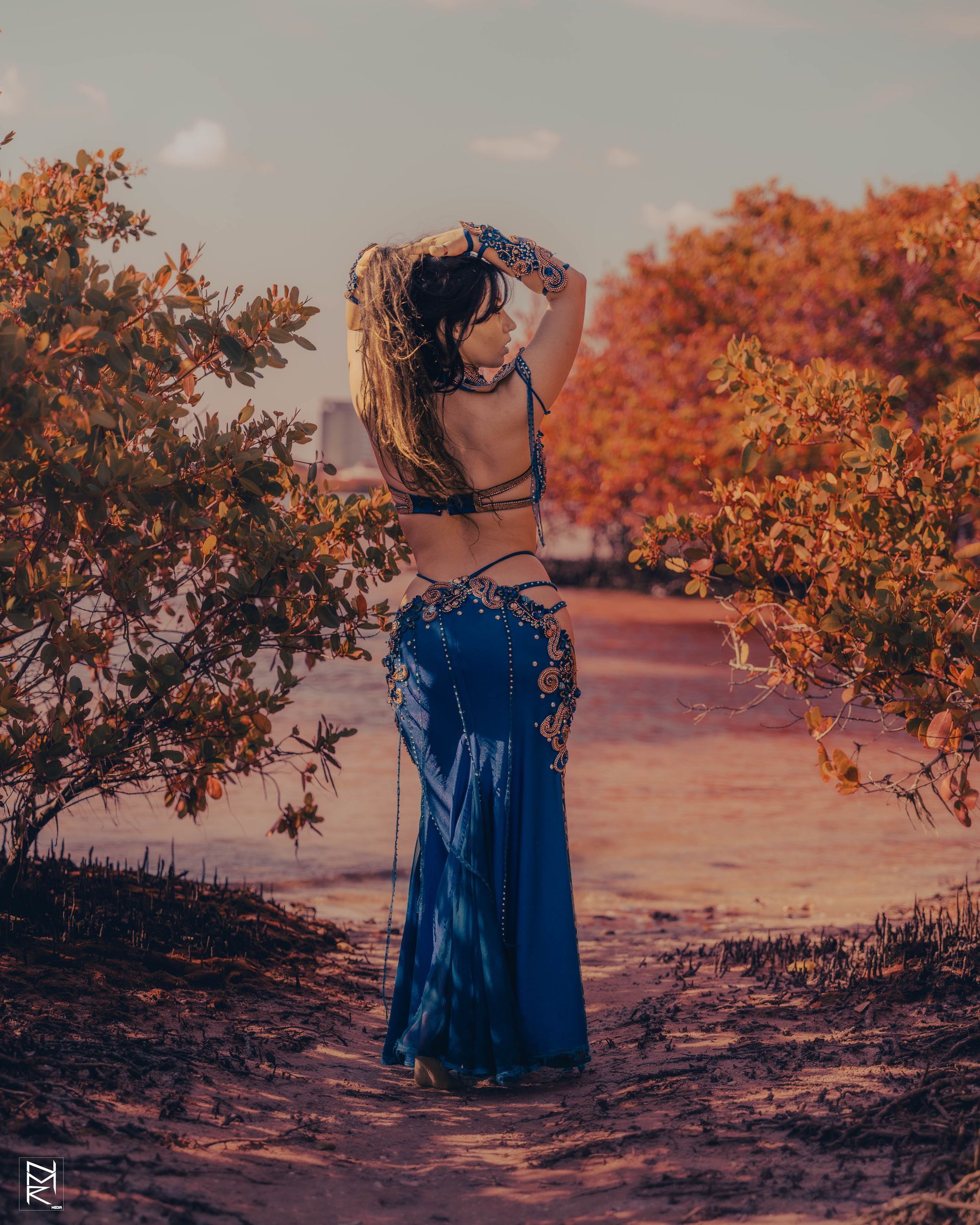 Belly dancer Azeeria Azizah in a blue dress is standing in front of a tree.