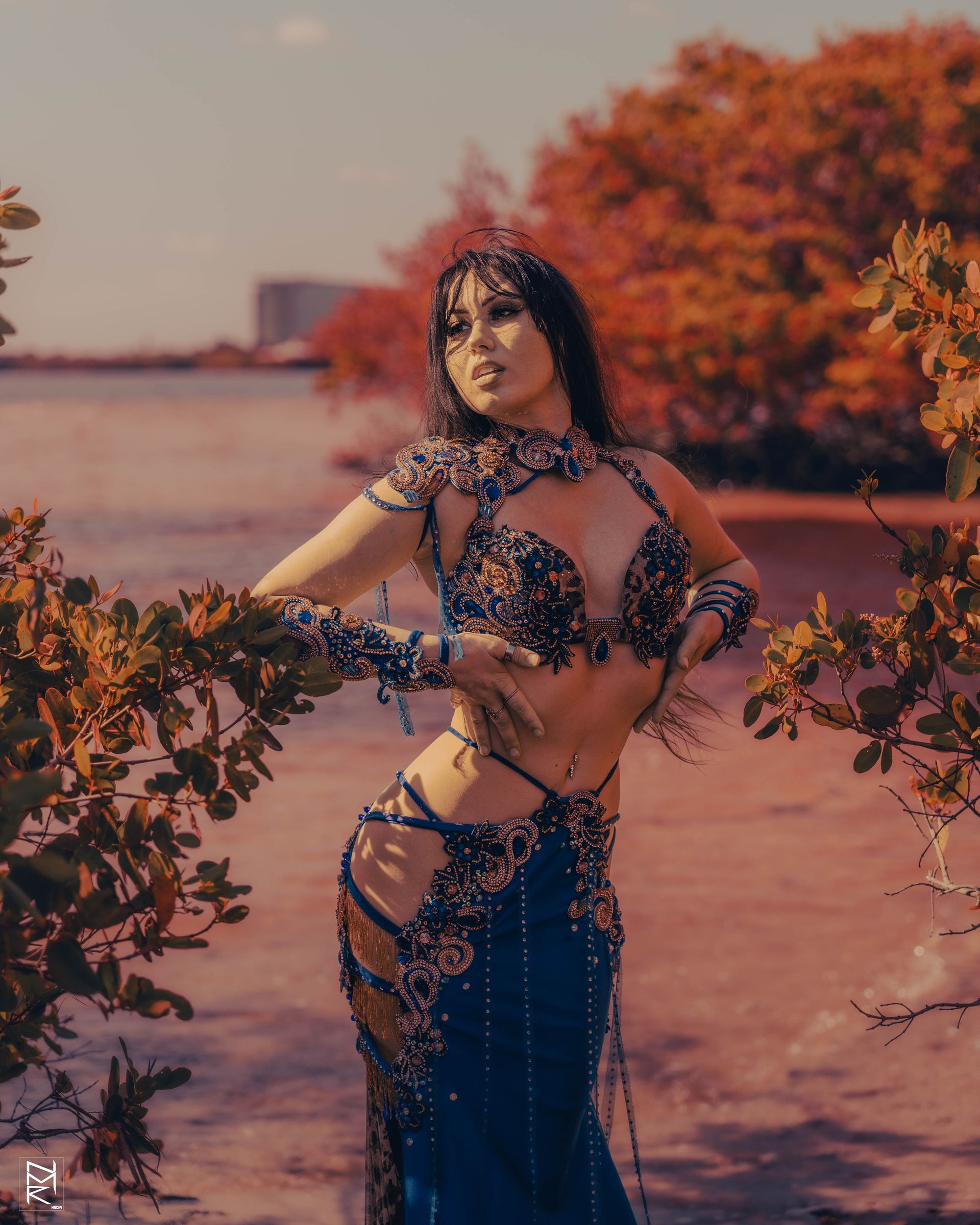 Azeeria Azizah in a belly dancer costume standing next to a tree posing.