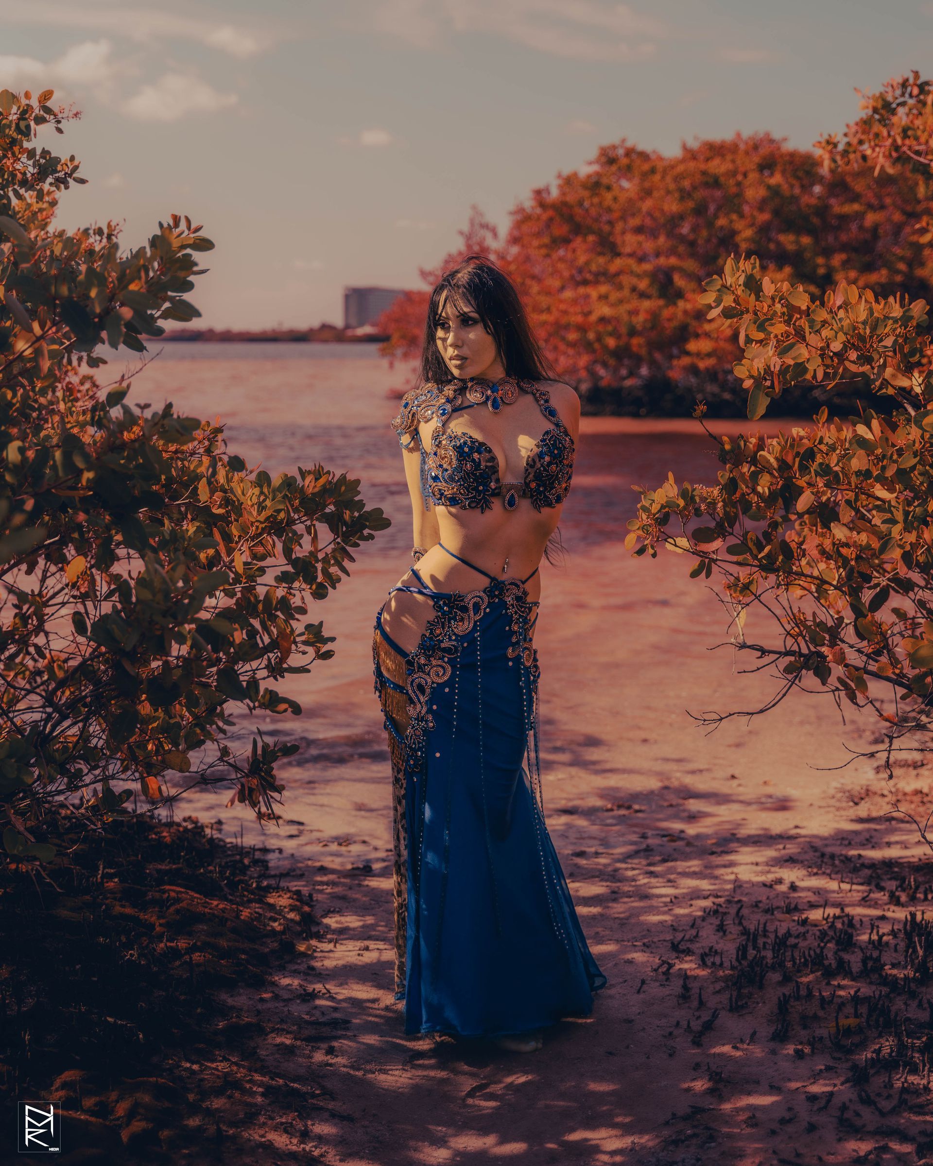 Azeeria Azizah in a blue dress is standing next to a tree.