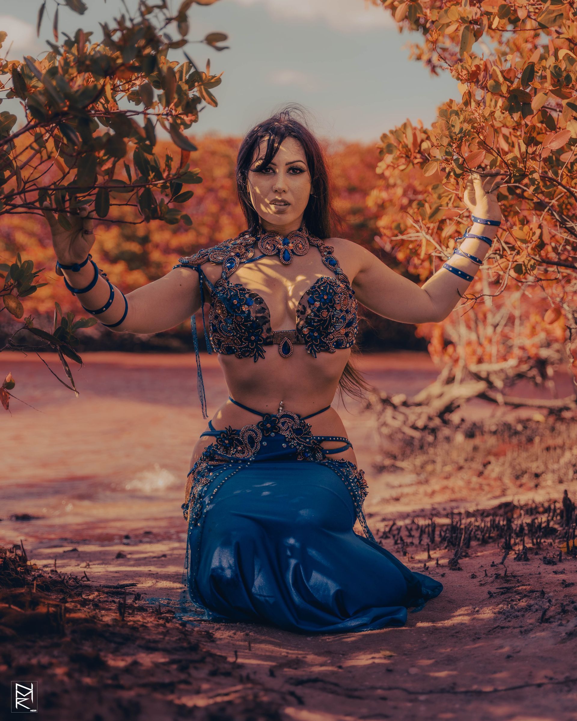 Belly dancer Azeeria Azizah kneeling down in the sand in front of a tree.