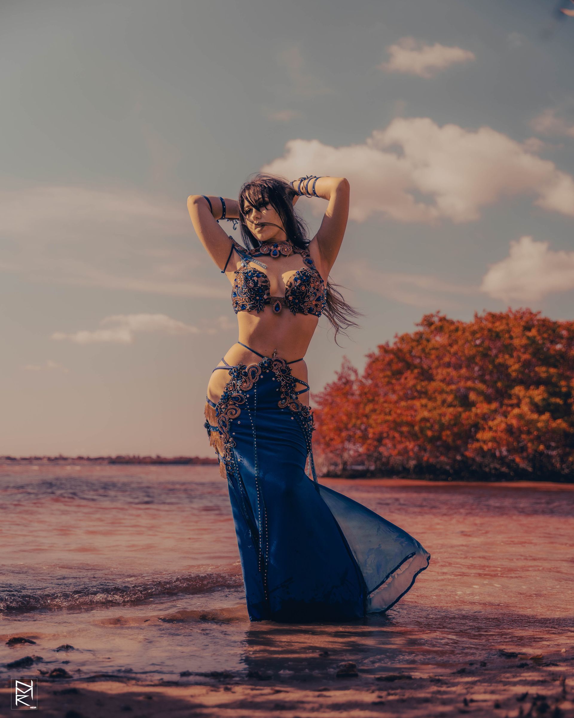Belly dancer Azeeria Azizah is standing in the water on the beach.