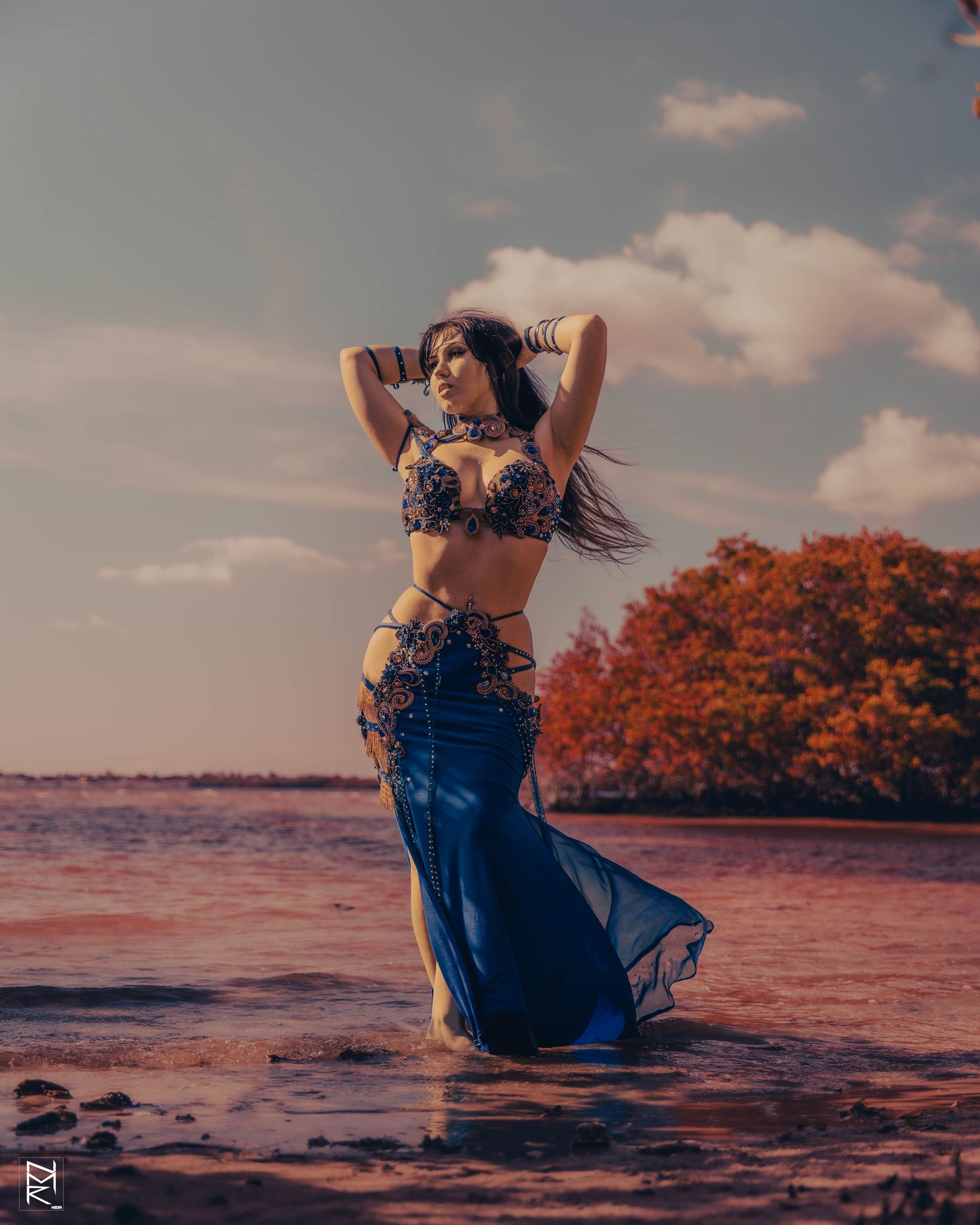 Belly dancer Azeeria Azizah in a blue dress is standing on the beach.