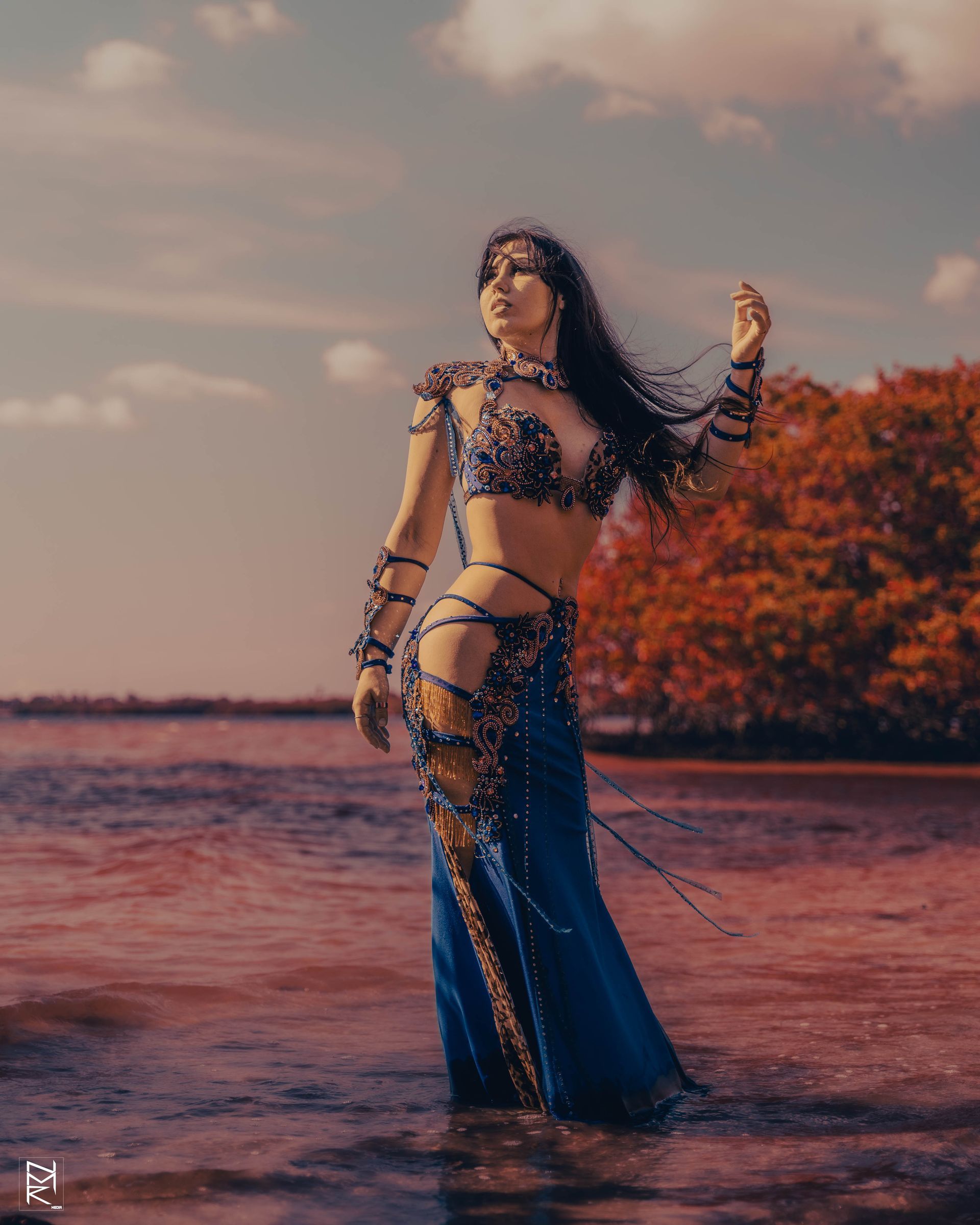 A photo of the Belly Dancer Azeeria Azizah gazing to the sun and holding her hair in the water at cypress beach, Tampa Fl