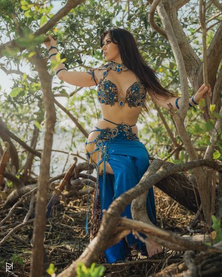 Belly dancer Azeeria Azizah in a belly dancer costume is standing in a tree.