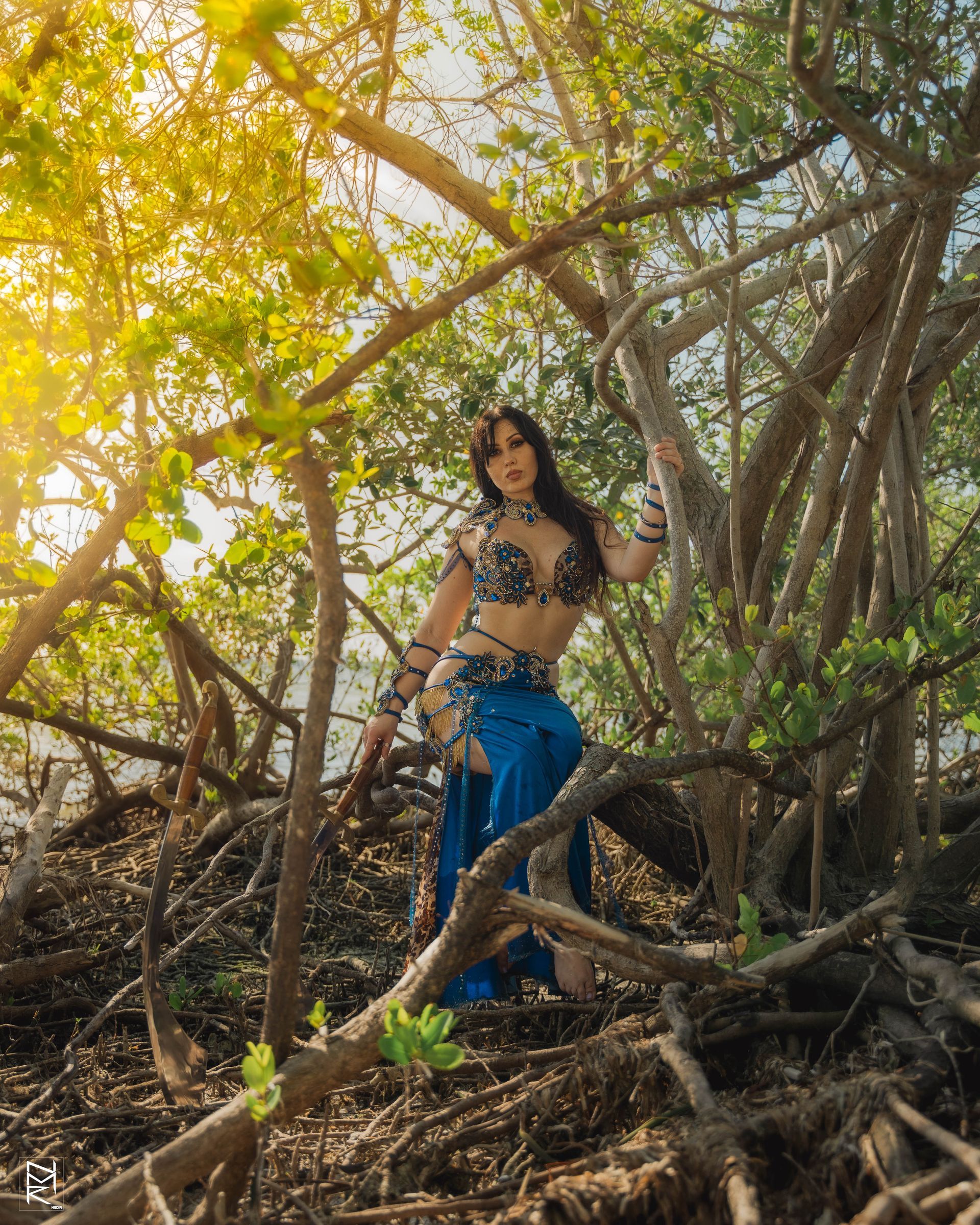 Belly dancer Azeeria Azizah in a belly dancer costume is standing in the woods.