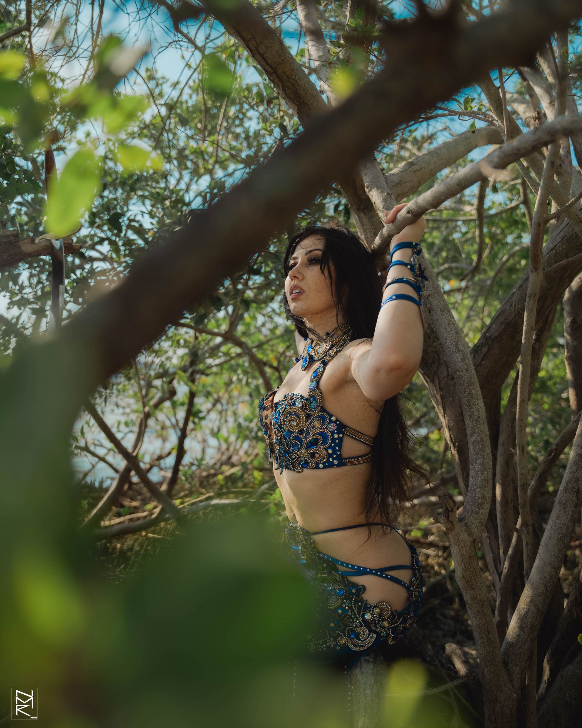 Belly dancer Azeeria Azizah in a bikini is standing in a tree.