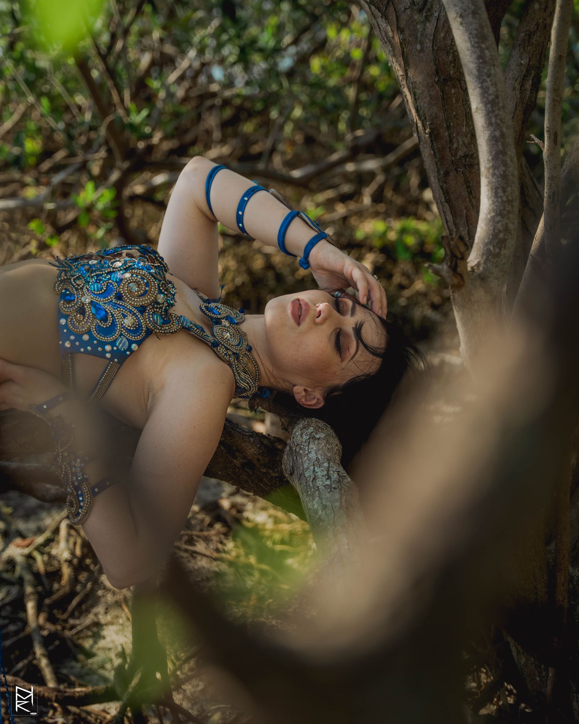 Belly dancer Azeeria Azizah in a blue top laying under a tree.