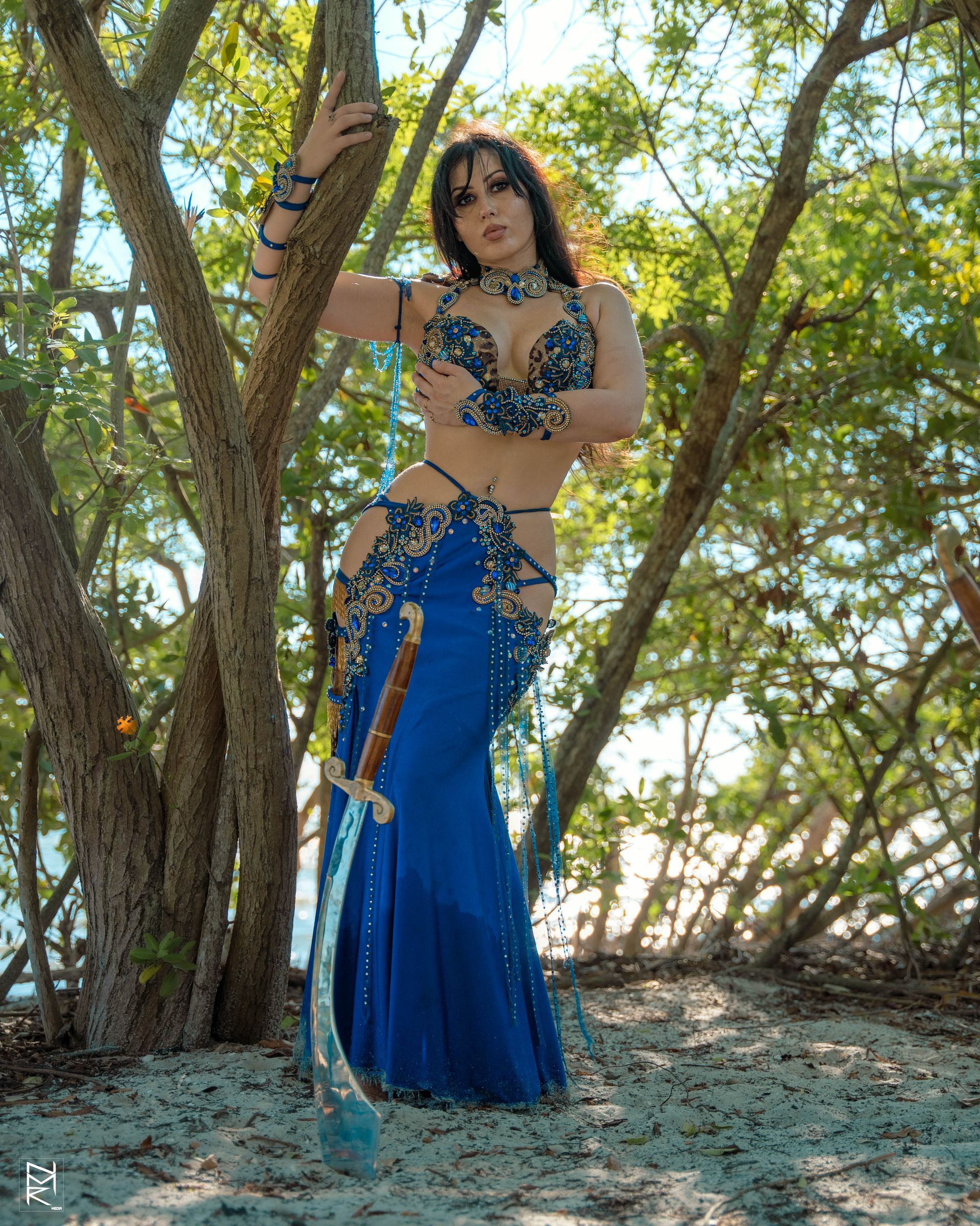 Belly dancer Azeeria Azizah in a blue dress standing in the woods.