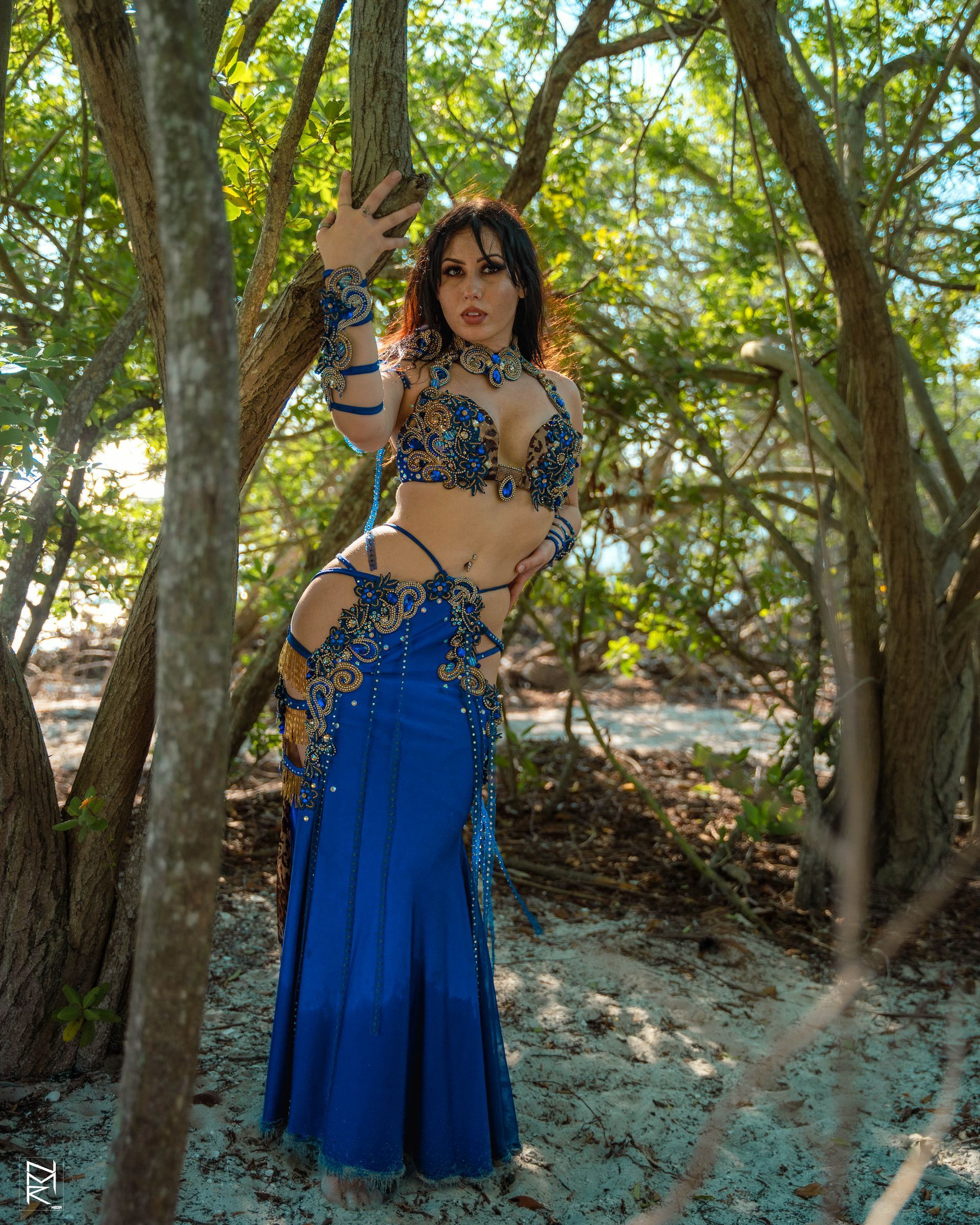 Belly dancer Azeeria Azizah in a blue dress standing next to a tree.