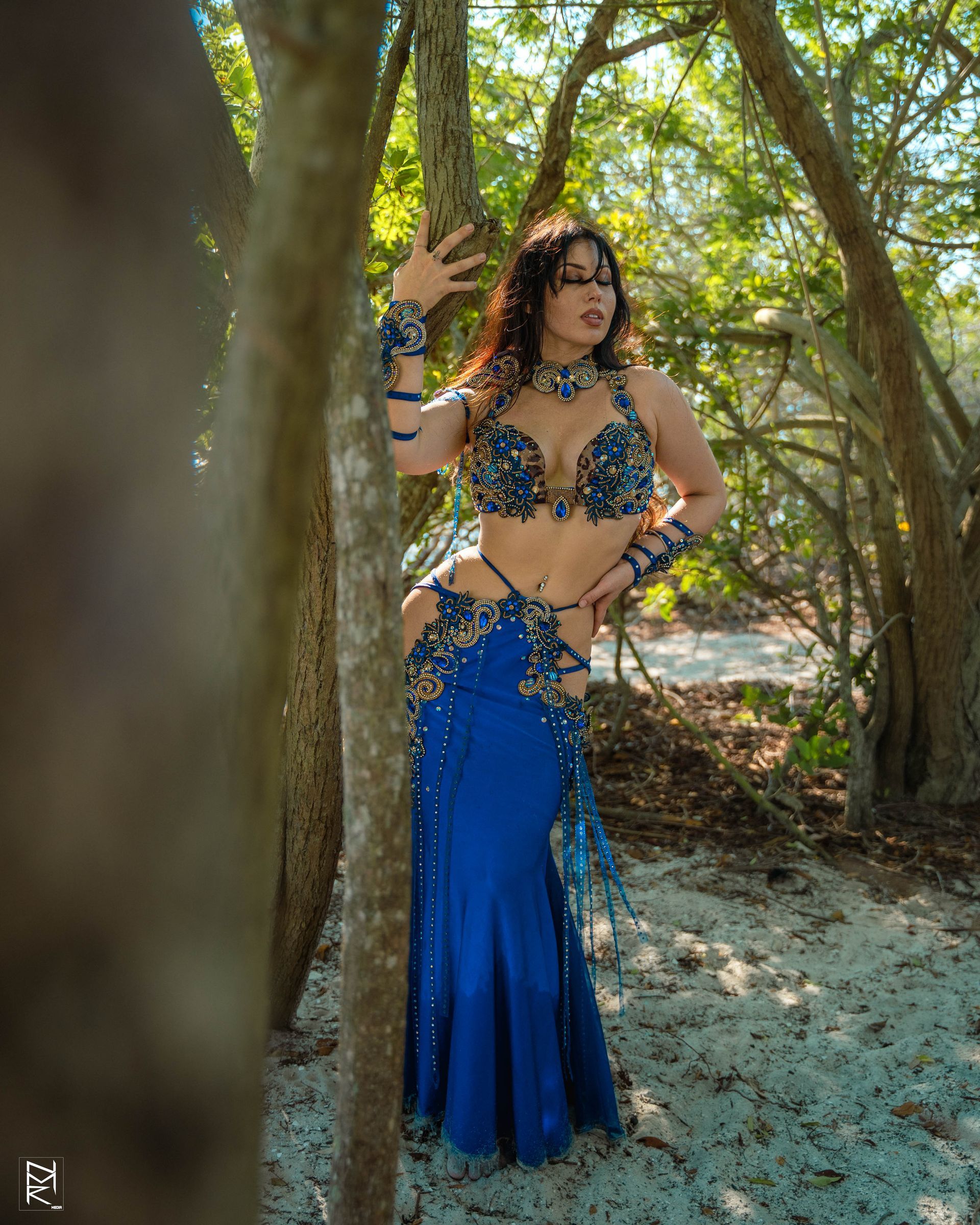 Belly dancer Azeeria Azizah in a blue belly dancer costume standing next to a tree.