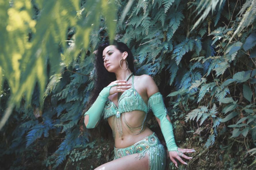 Belly dancer Azeeria Azizah in a green costume is standing in the woods in Puerto Rico. 