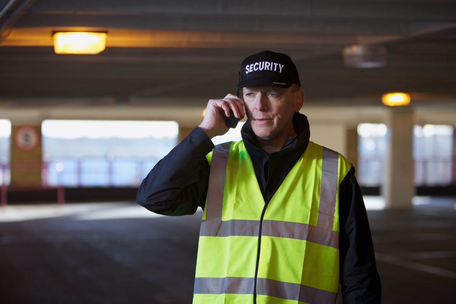 A security guard is using a walkie-talkie in a parking building.
