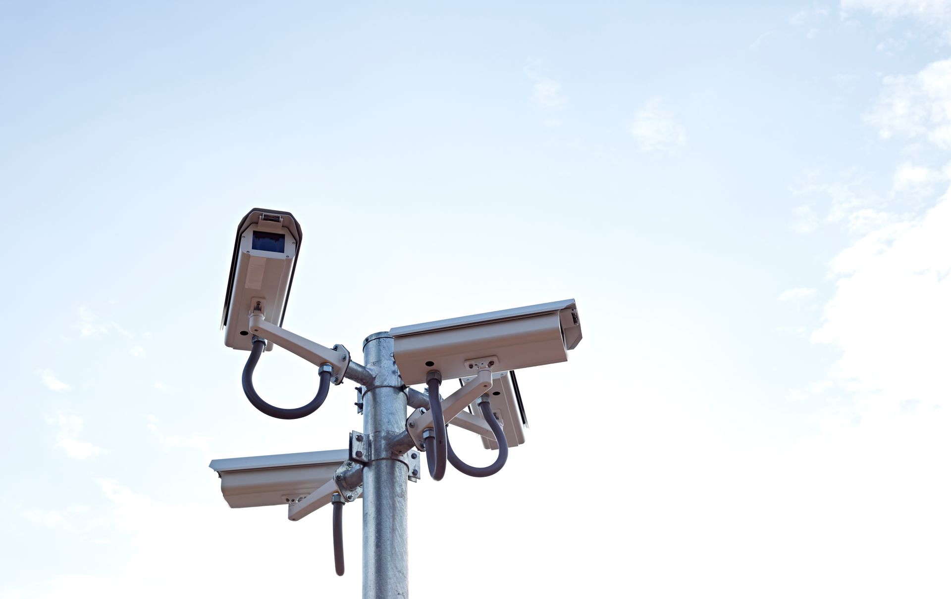 Security cameras mounted on a pole against a pale blue sky. Security cameras mounted on a pole against a pale blue sky.