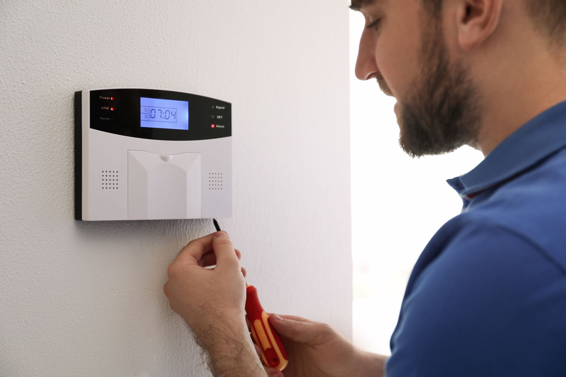 A technician installing a home security system on a white wall in a home. A technician installing a home security system on a white wall in a home.