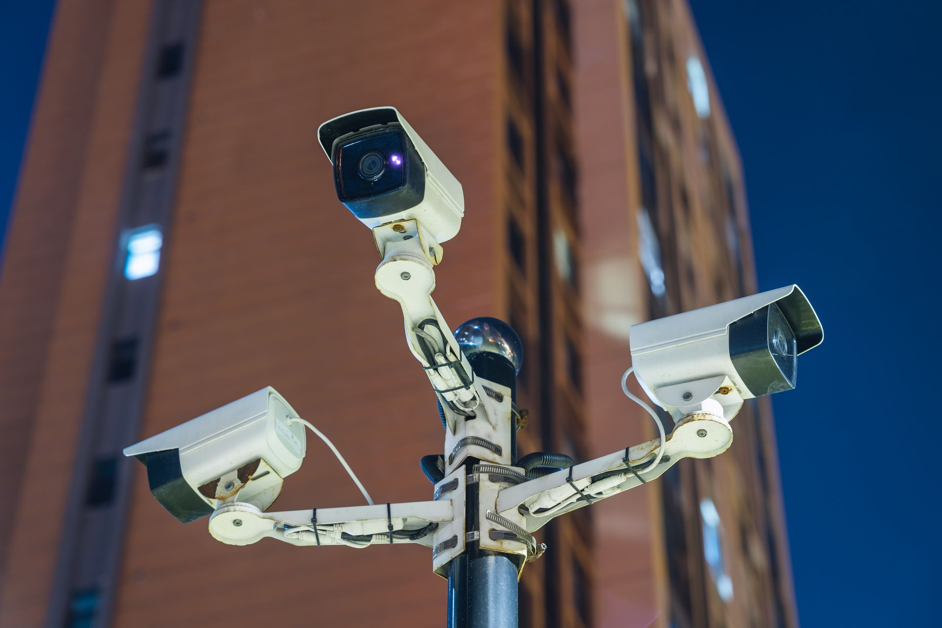 Three security cameras on a pole, overlooking a building at night.