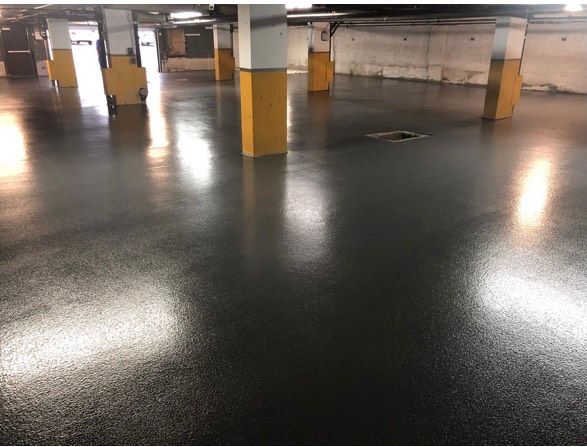 Un parking souterrain lumineux, doté d'un sol lisse gris foncé et de piliers blancs à base jaune.