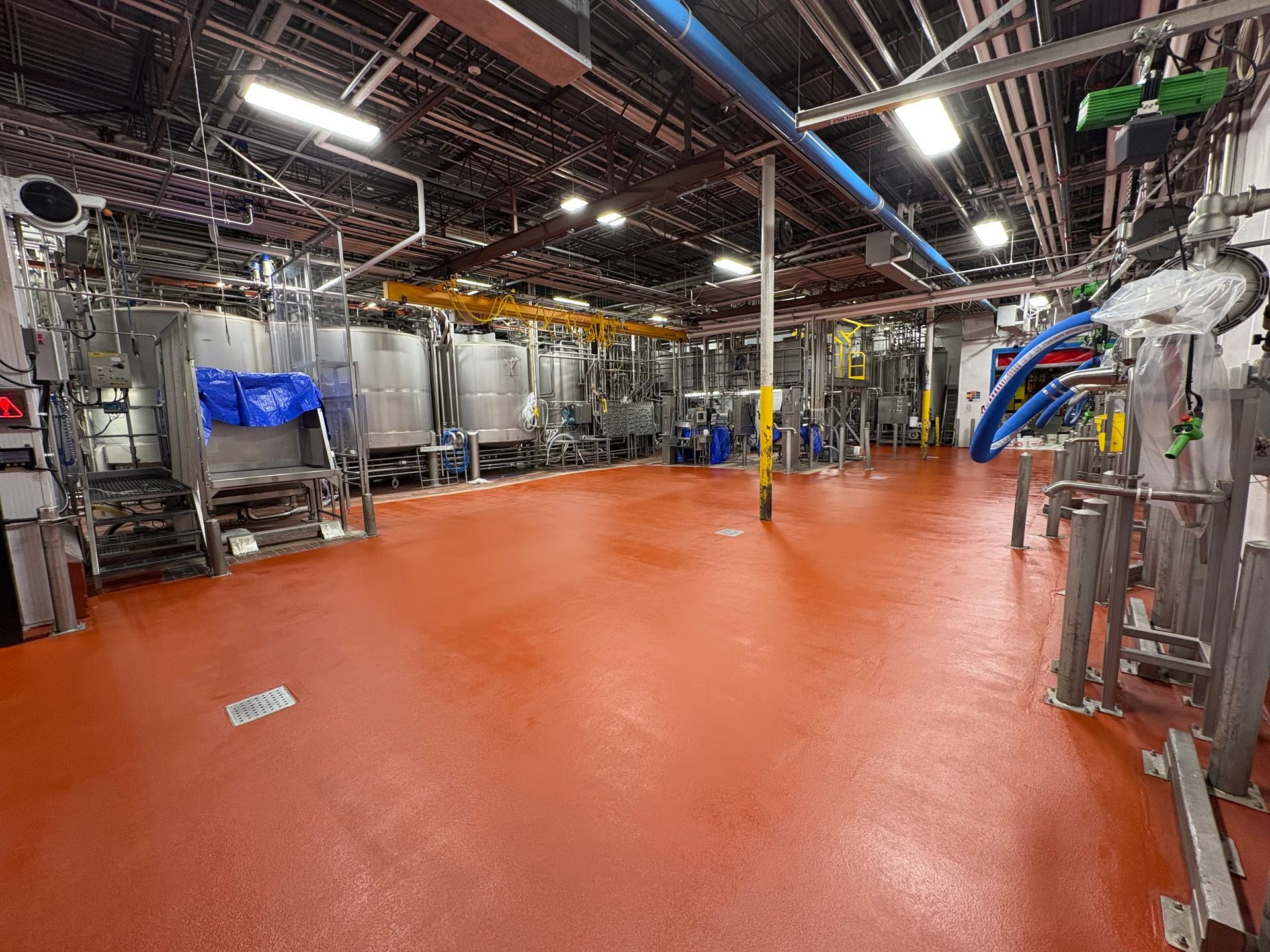 Vue d'ensemble d'une installation de fabrication industrielle présentant de grandes cuves en acier et un sol lisse en époxy orange.