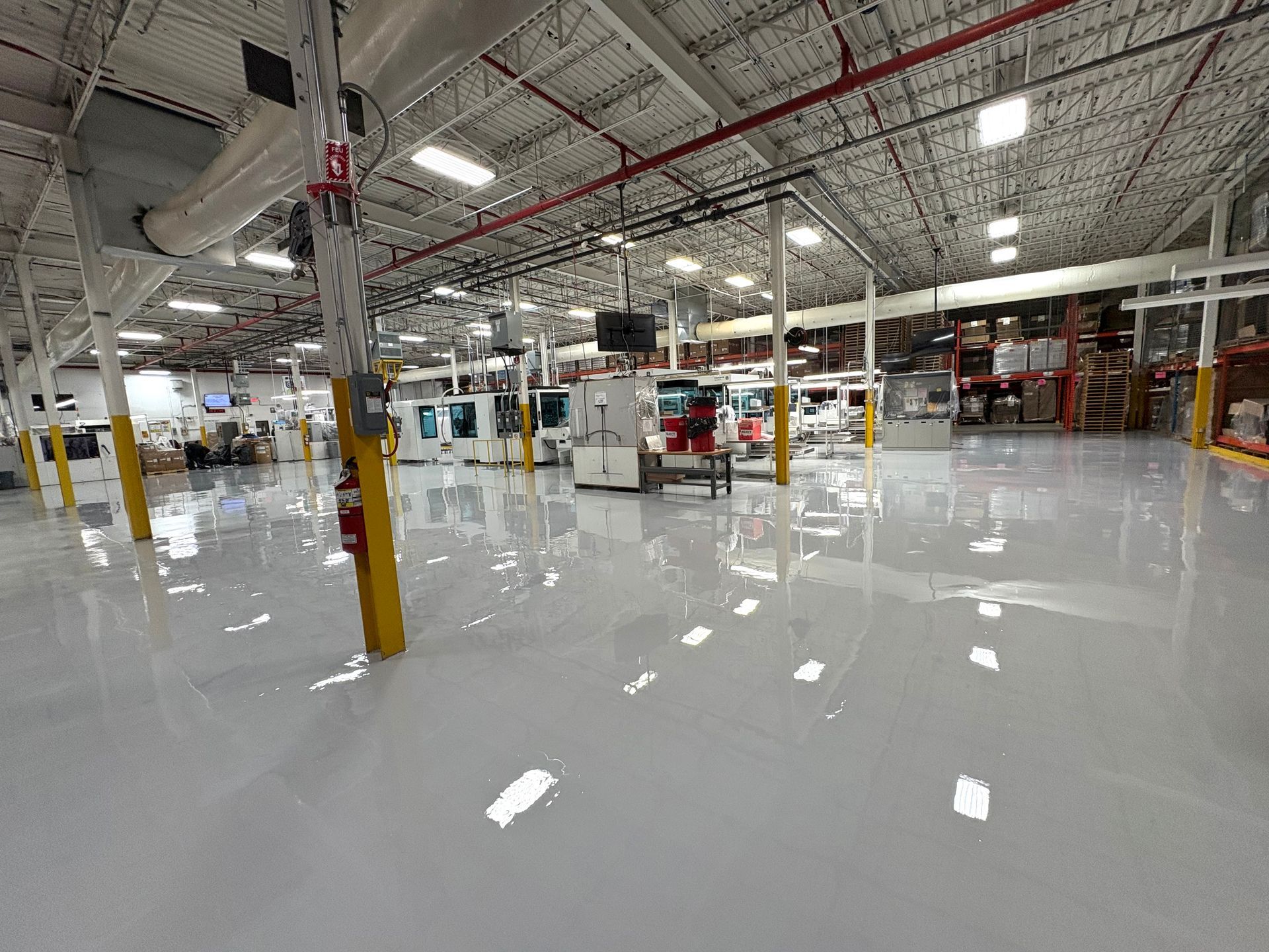 Un intérieur d'entrepôt lumineux et propre, avec un sol en époxy gris poli, un plafond blanc et des colonnes de soutien jaunes.