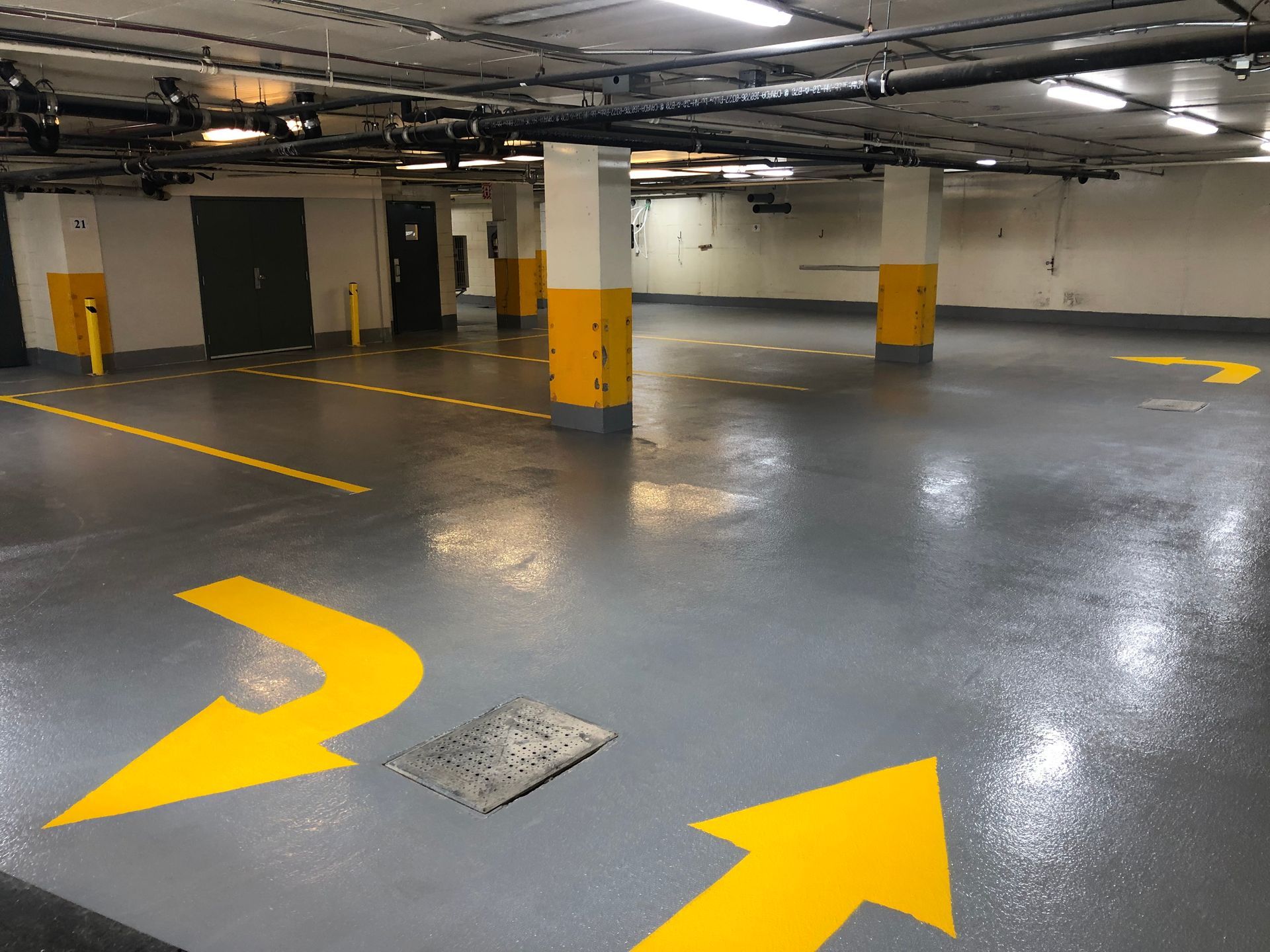 Empty, gray parking garage with yellow directional arrows and support pillars.
