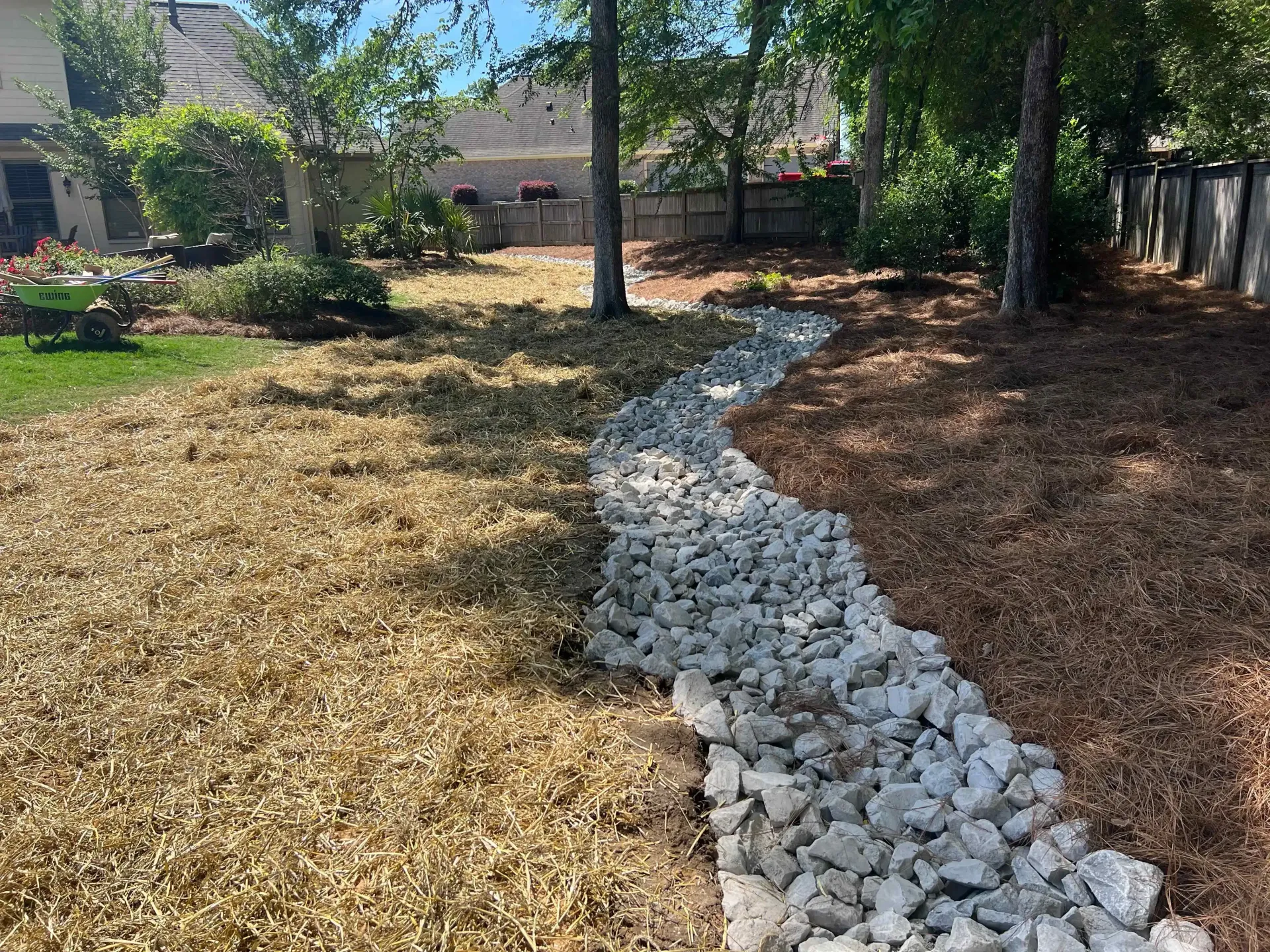 A white gravel drainage system winds along the side of a house, surrounded by grass.