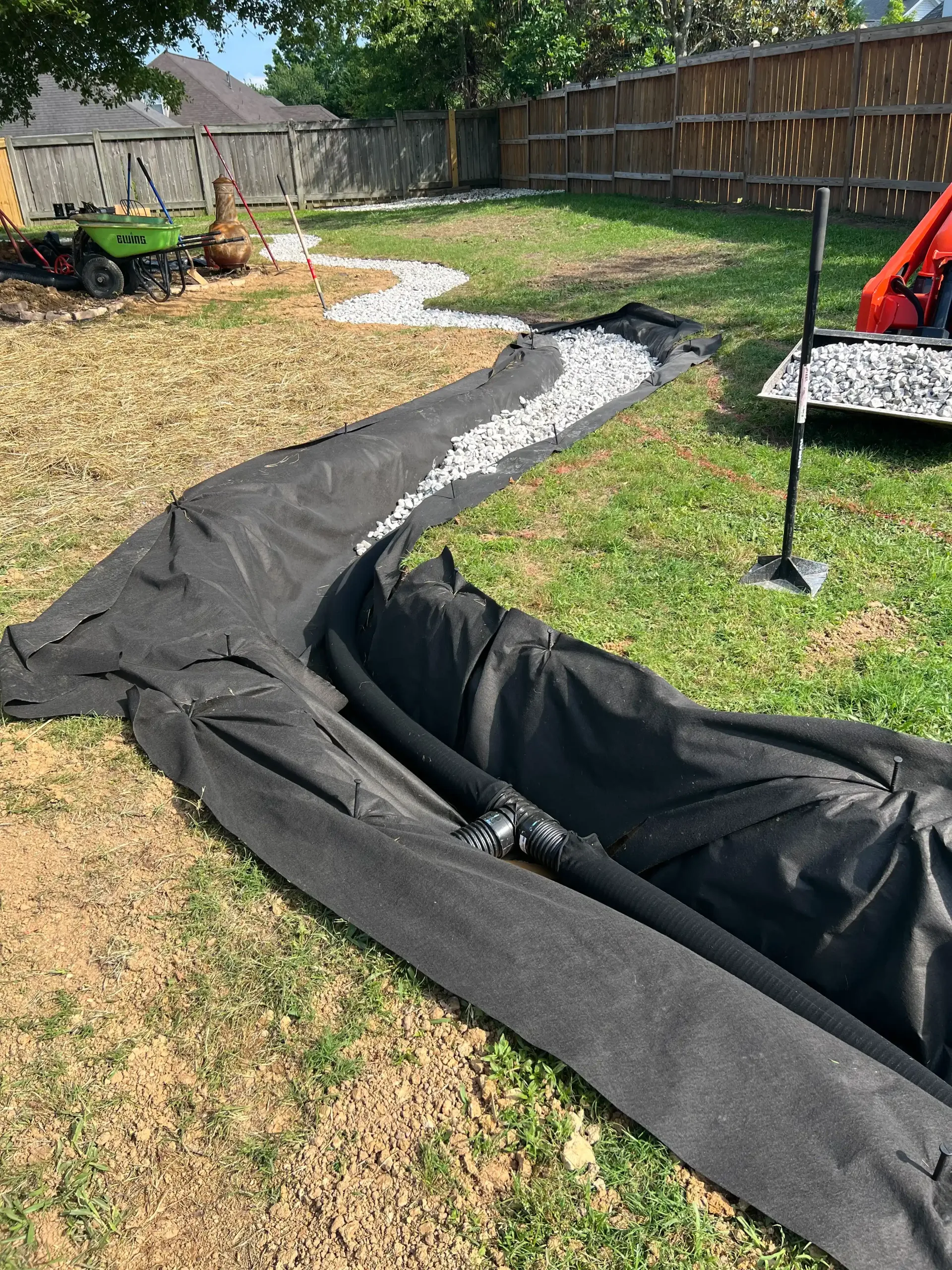 Black fabric and gravel in a trench, likely for drainage, in a grassy backyard.
